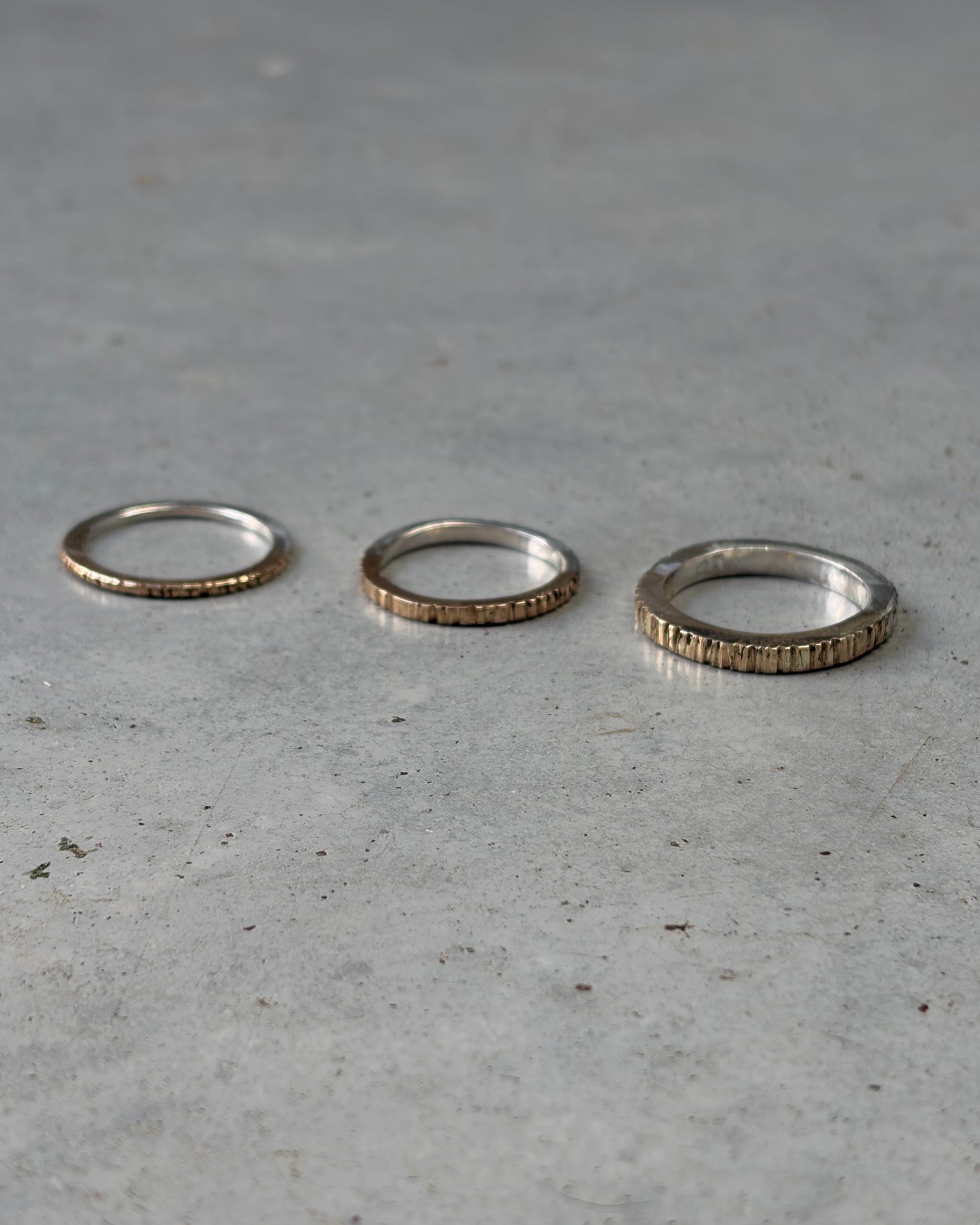 Three textured metal rings in graduated sizes arranged horizontally on a gray concrete surface.