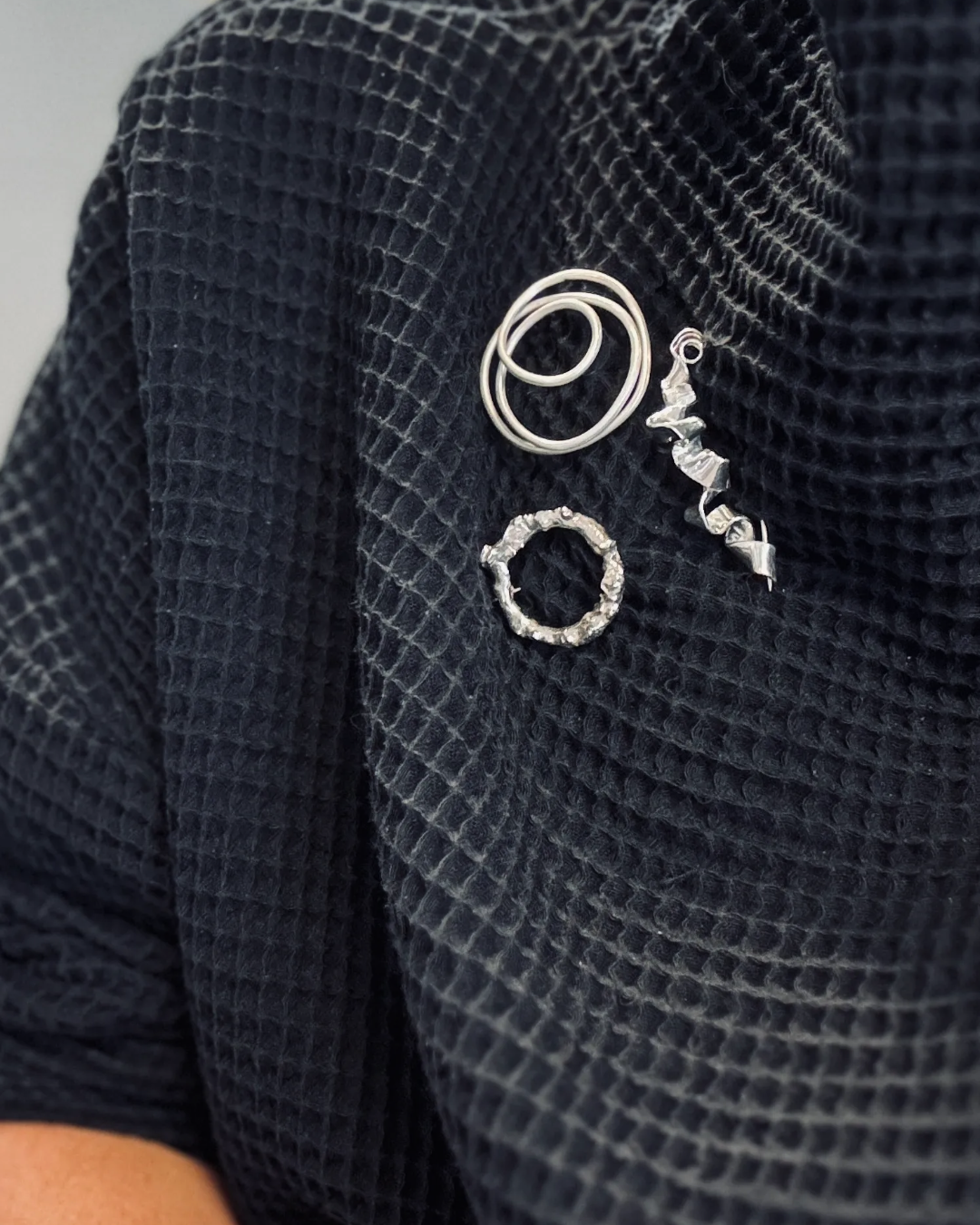 Three sculptural silver brooches on a woman’s black shirt.