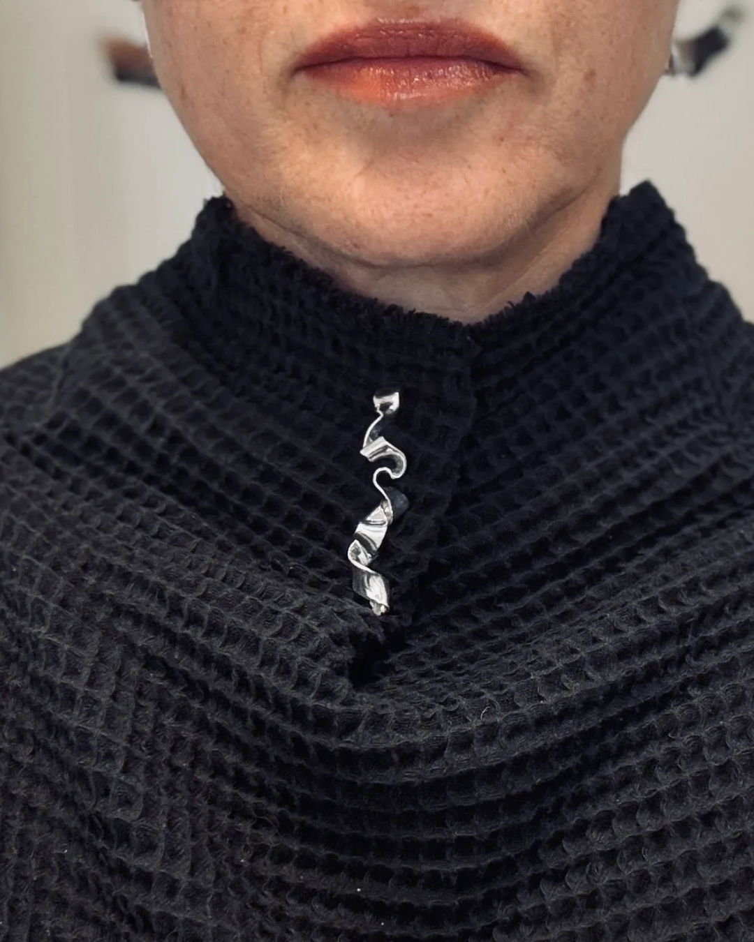 Person wearing a dark textured sweater with a decorative brooch on a neutral background