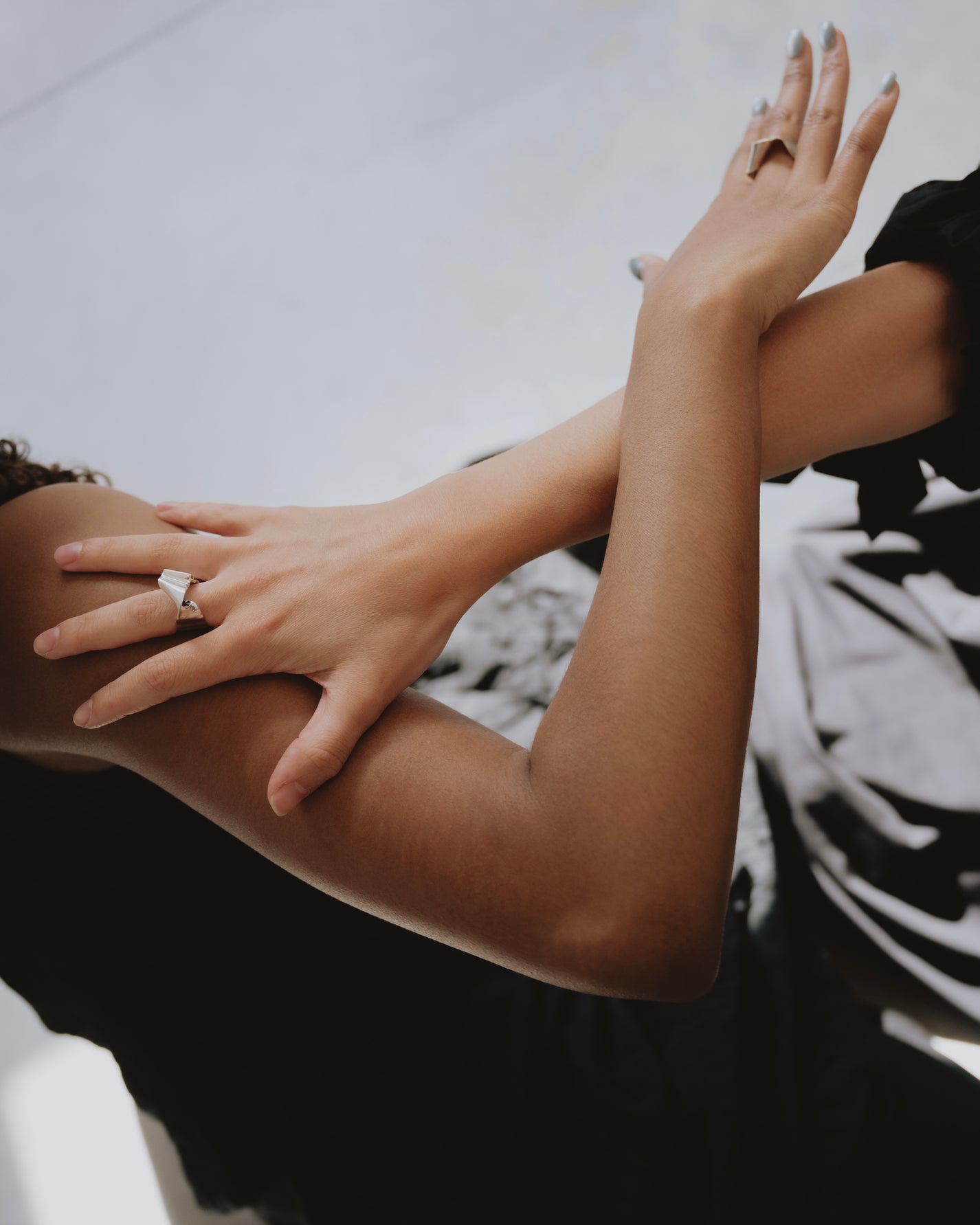 A close-up lifestyle shot of a person wearing a silver ring with a large clear gemstone on their index finger, with their other hand resting on their shoulder against a black and white patterned background.