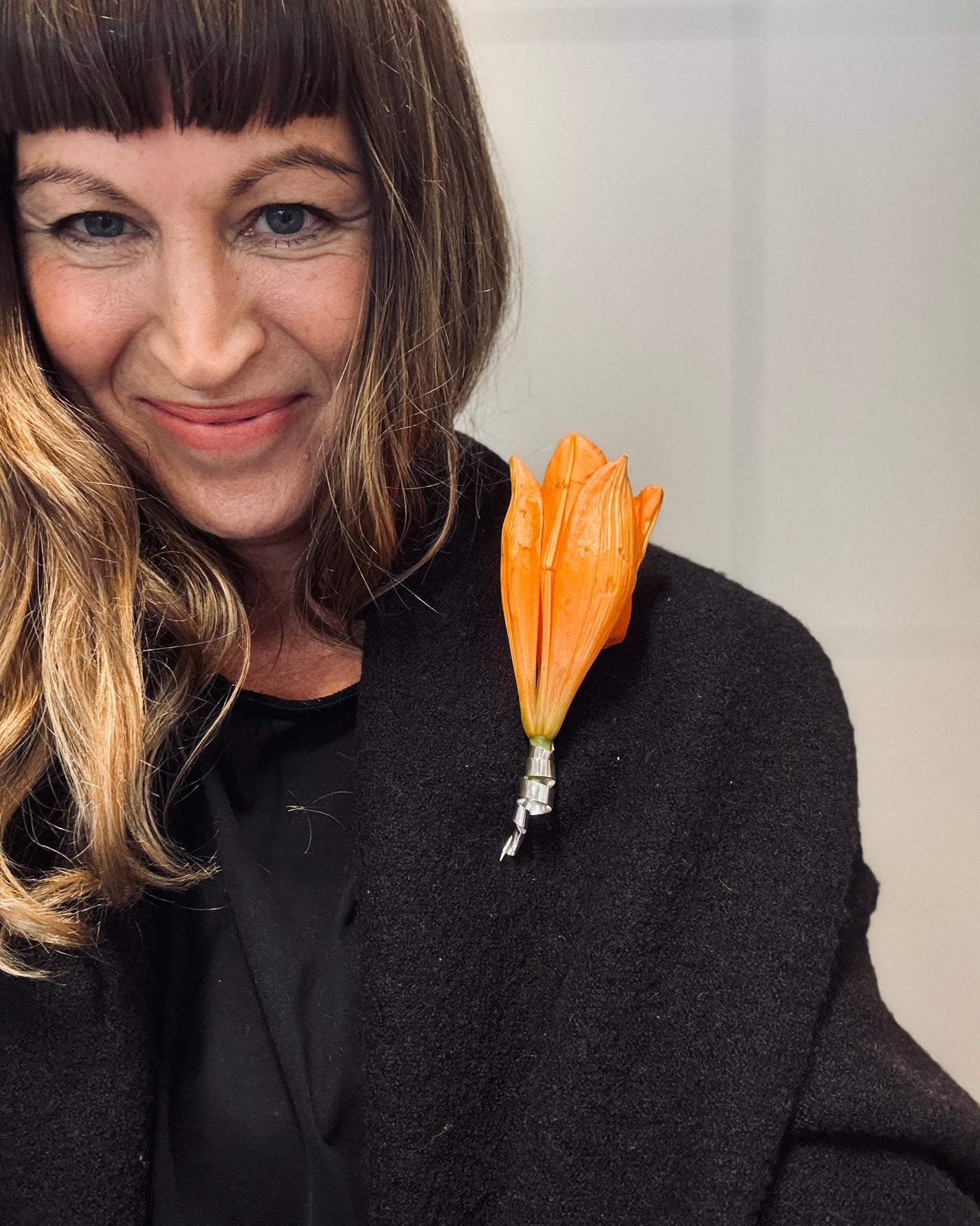 Woman wearing a black coat with an orange flower accessory on a plain background