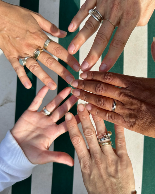 Five hands touching fingers with rings on and green and white stripes in background.