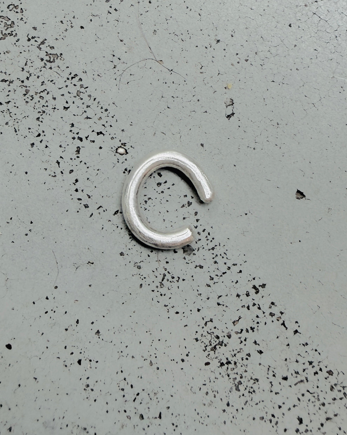 A small silver metal C-shaped ring or clasp lies on a speckled gray surface.