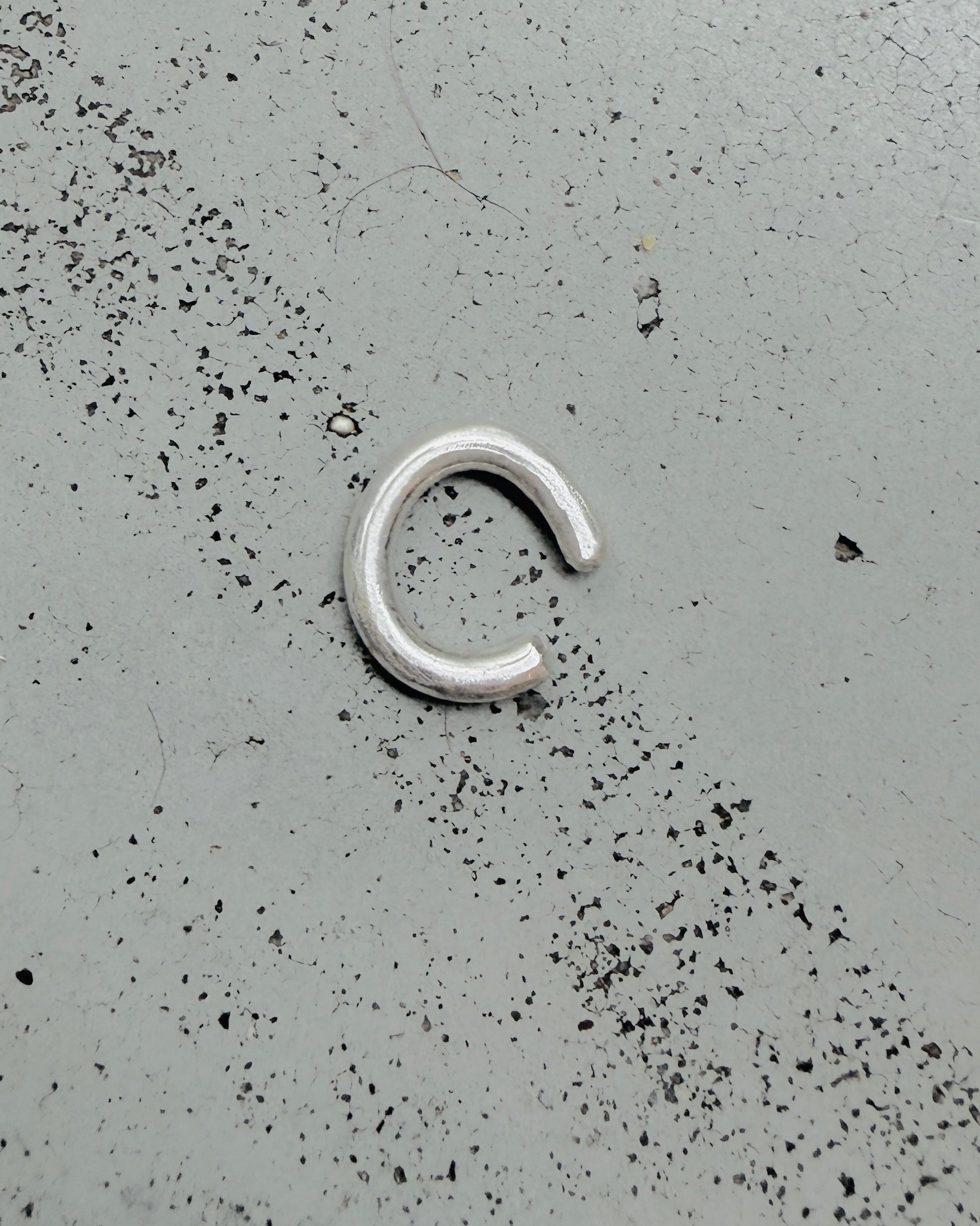 A small silver metal C-shaped ring or clasp lies on a speckled gray surface.