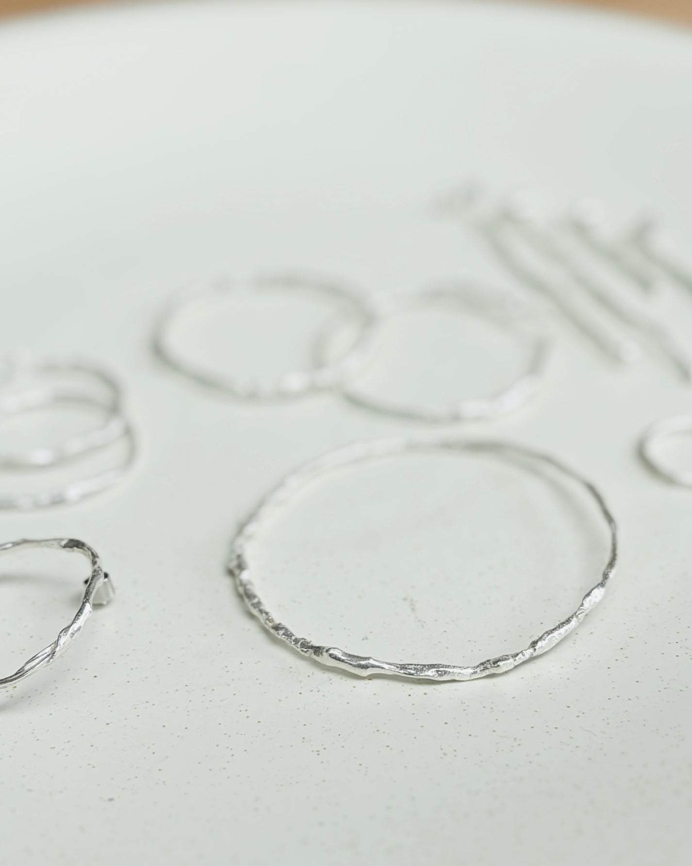 A close-up of several thin silver rings with a hammered or textured finish, arranged on a light off-white surface.
