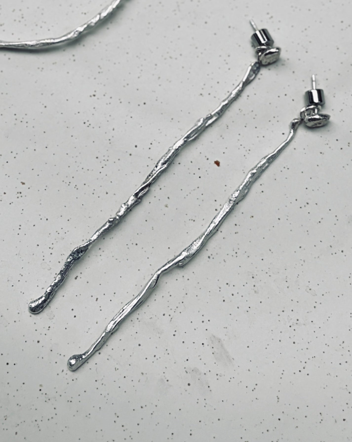 A jewelry set featuring a large textured silver hoop, a smaller textured silver hoop, a smaller textured silver hoop, and two long textured silver drop earrings, arranged on a light gray speckled surface.