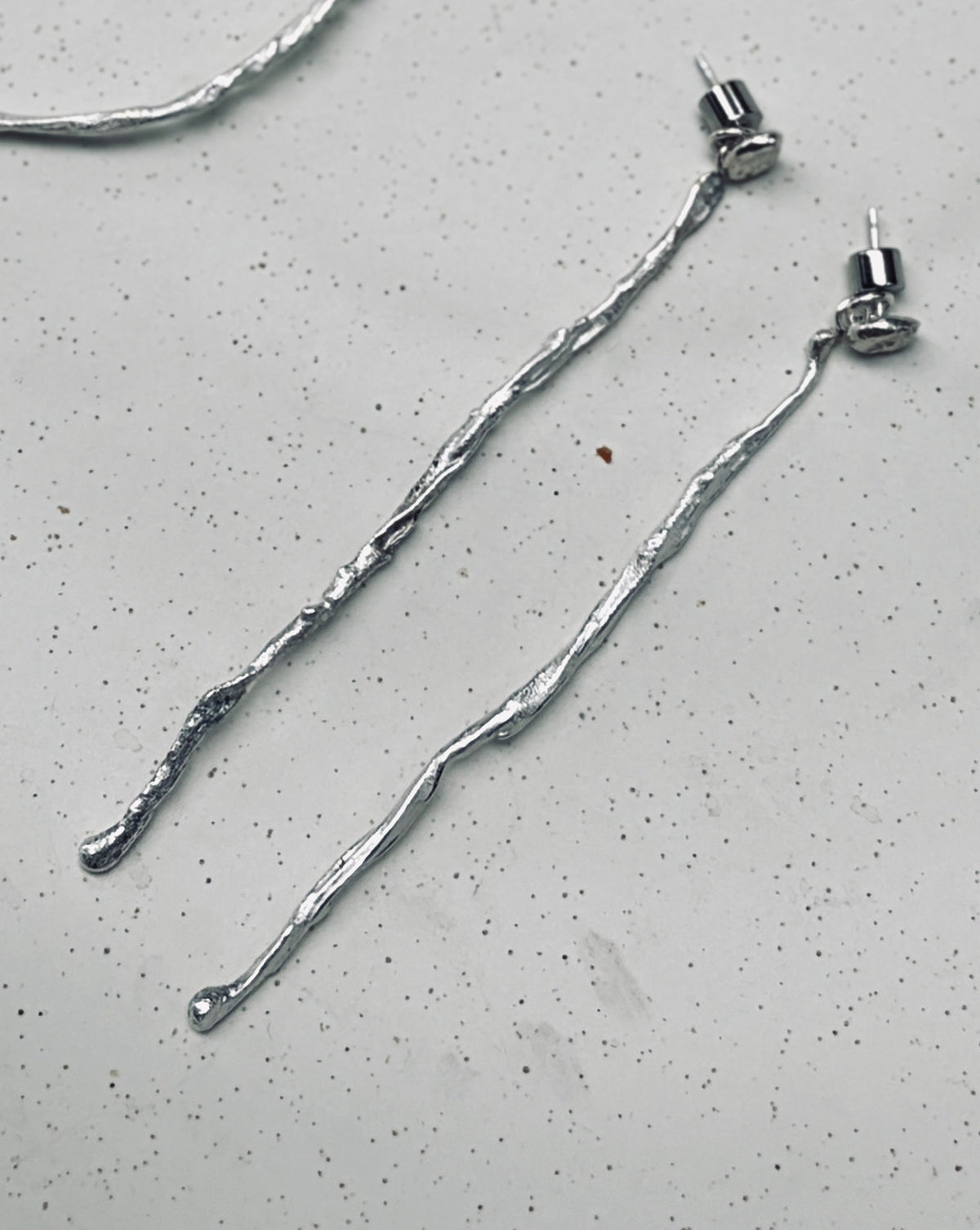 A jewelry set featuring a large textured silver hoop, a smaller textured silver hoop, a smaller textured silver hoop, and two long textured silver drop earrings, arranged on a light gray speckled surface.