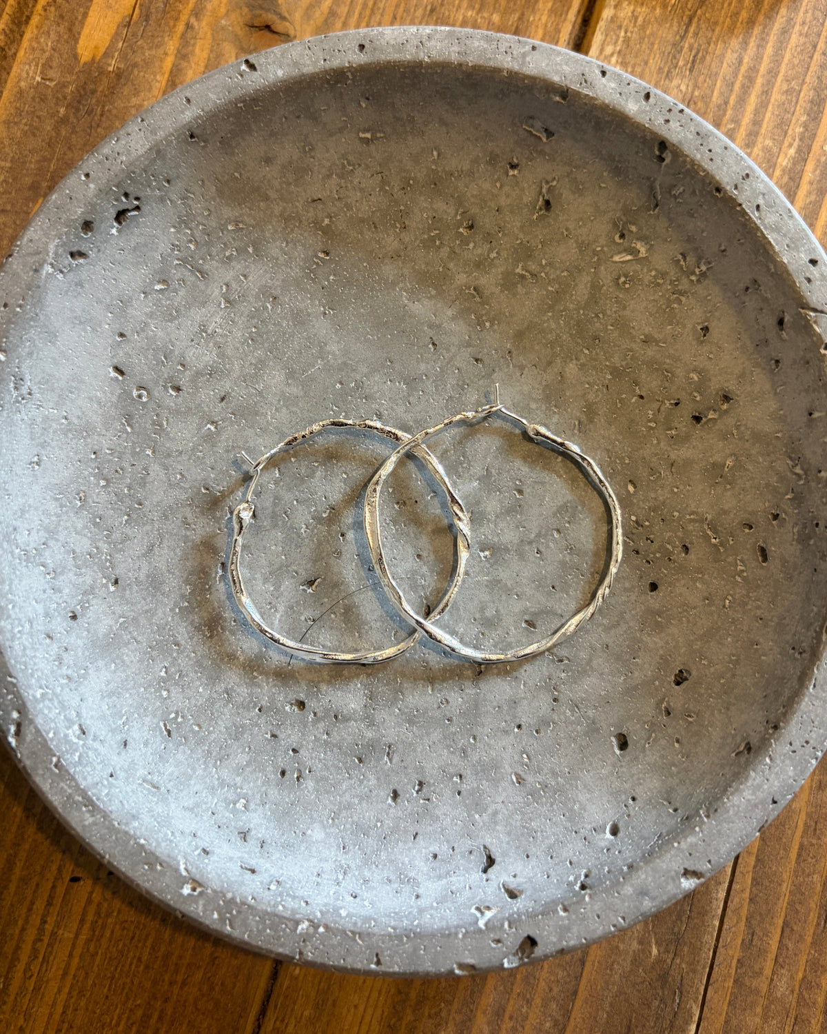 Two thin silver-toned wire rings resting inside a round textured gray concrete dish on a wooden surface.