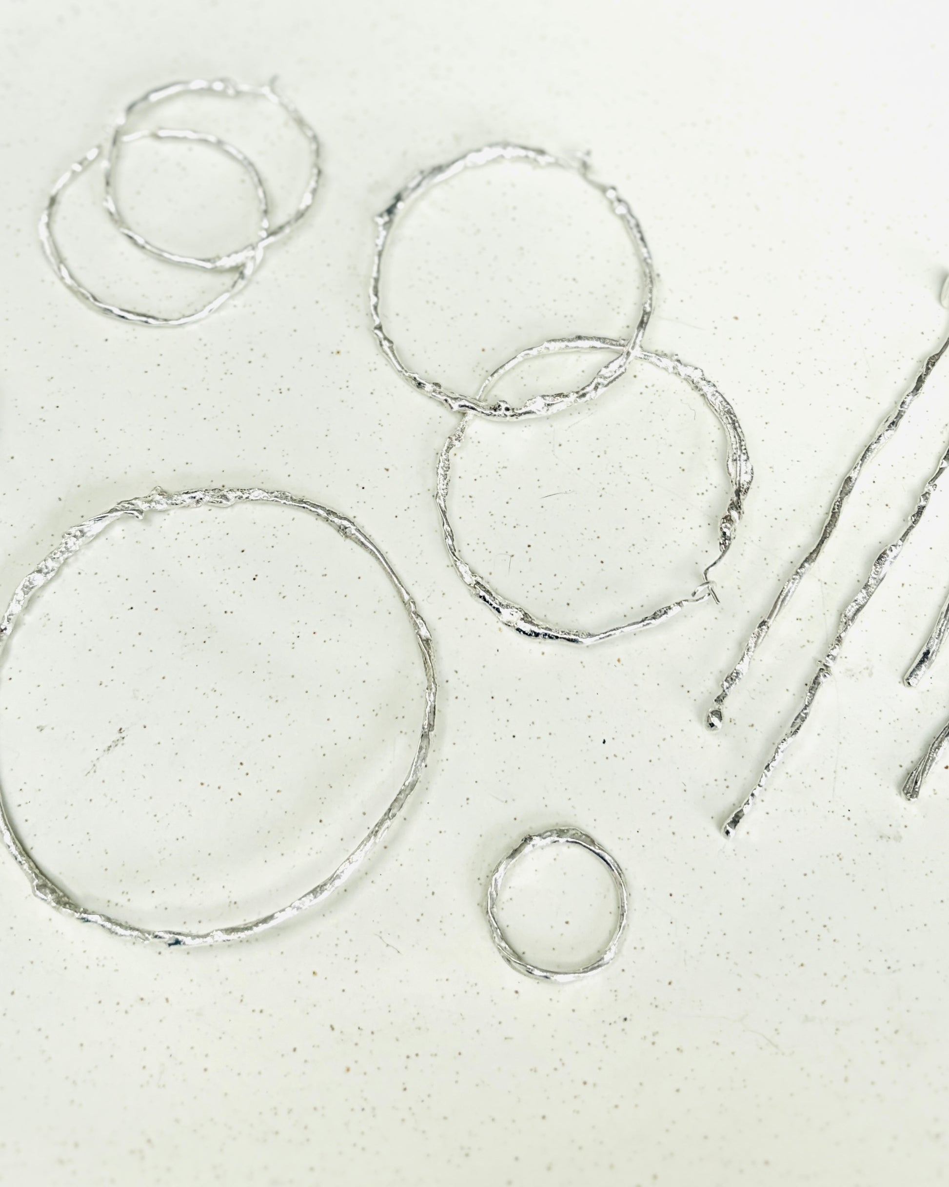 A set of handmade silver hoop earrings with a textured, hammered finish, displayed on a light speckled surface.