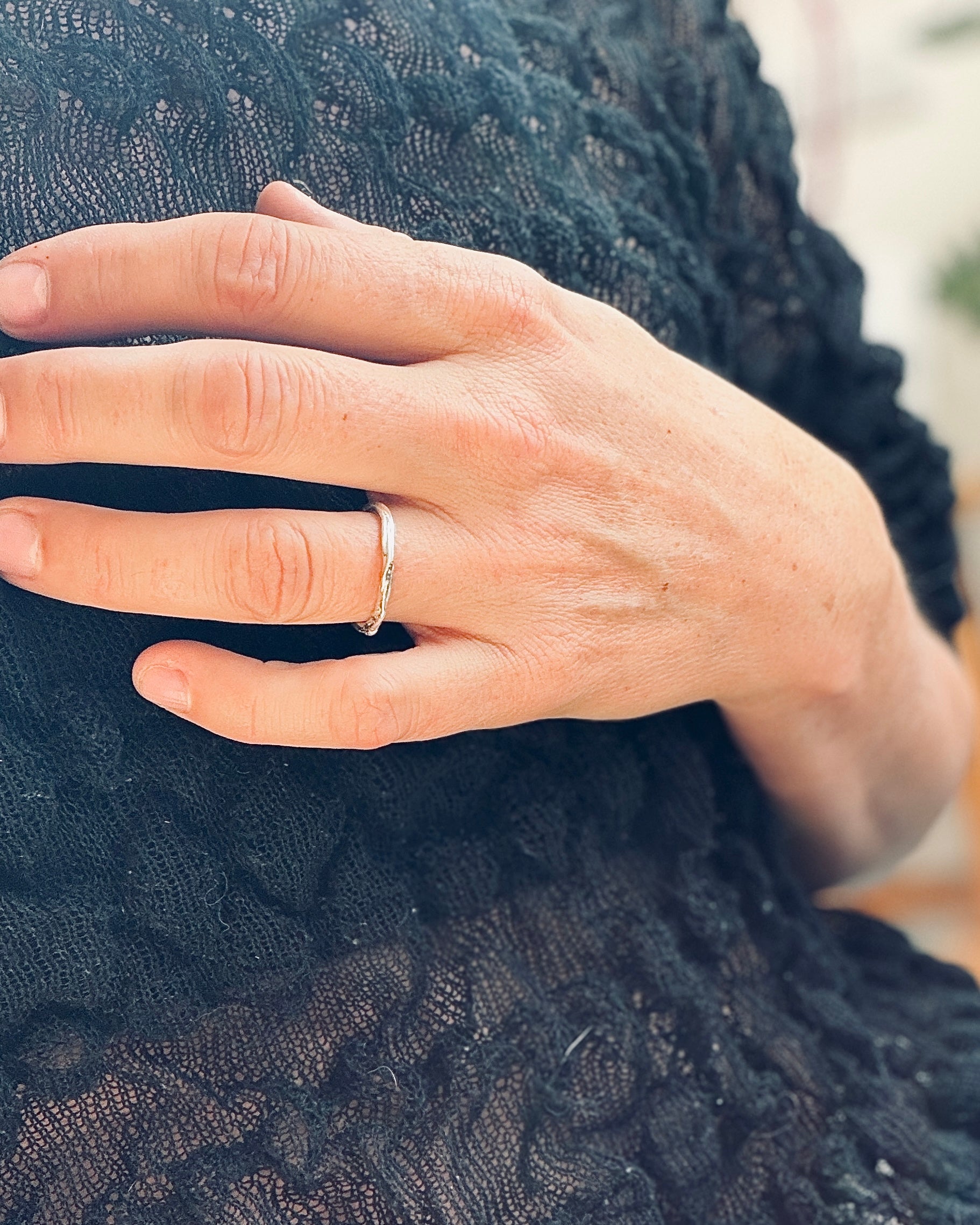 A close-up of a person's hand wearing a thin silver band ring, resting on a black lace garment.
