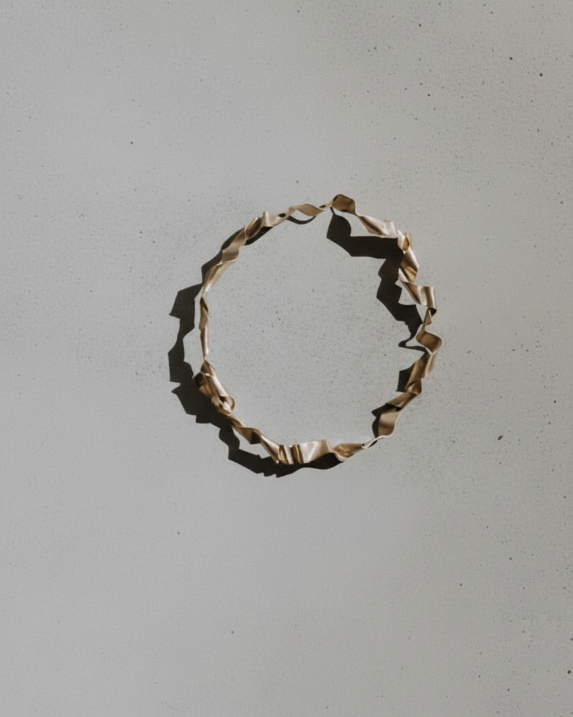 A single twisted, frayed beige cord or ribbon loop lies on a plain light gray surface, casting a dark shadow to the left.