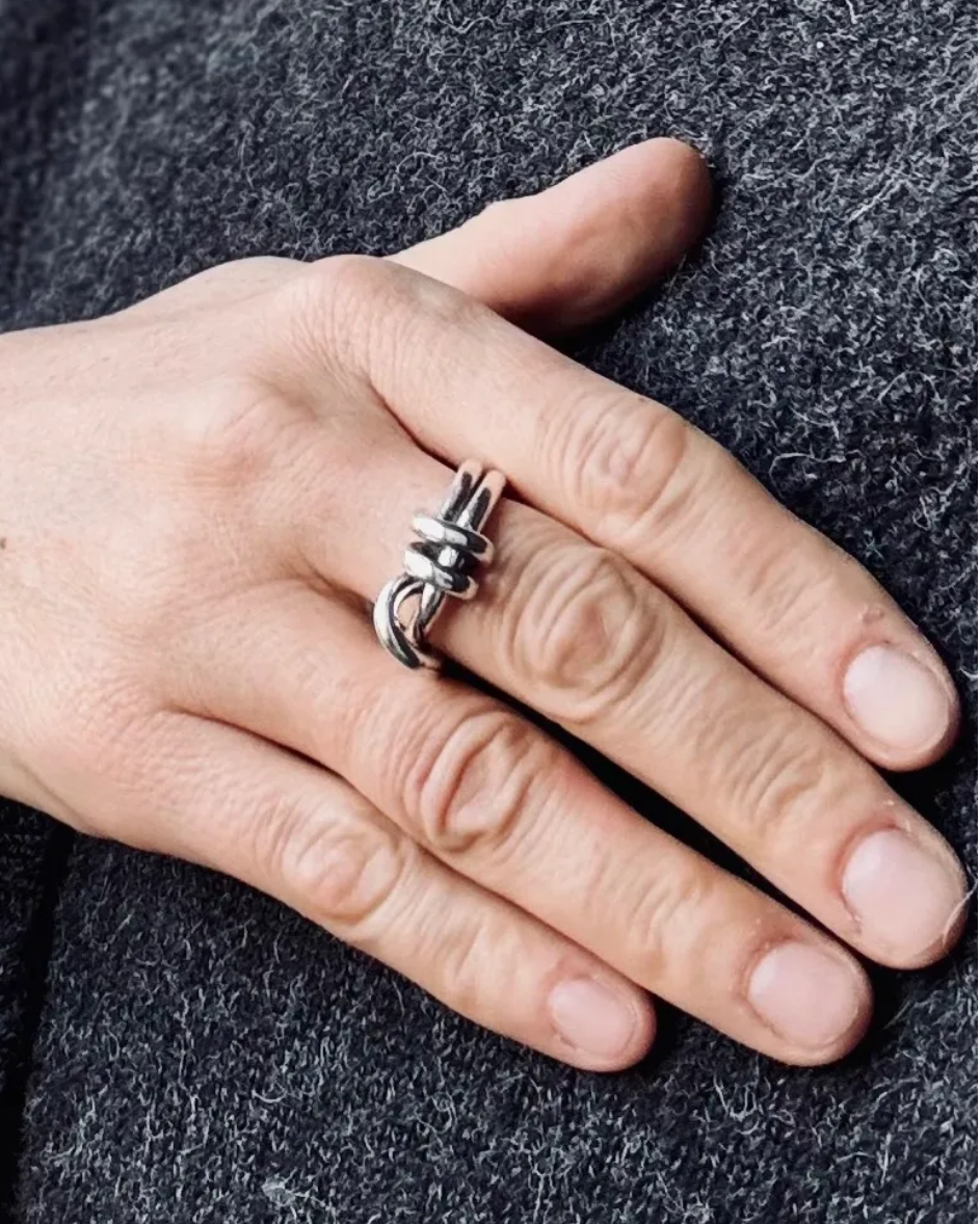 A close-up of a hand wearing a silver ring with a twisted knot design, resting on a dark gray textured knit surface.