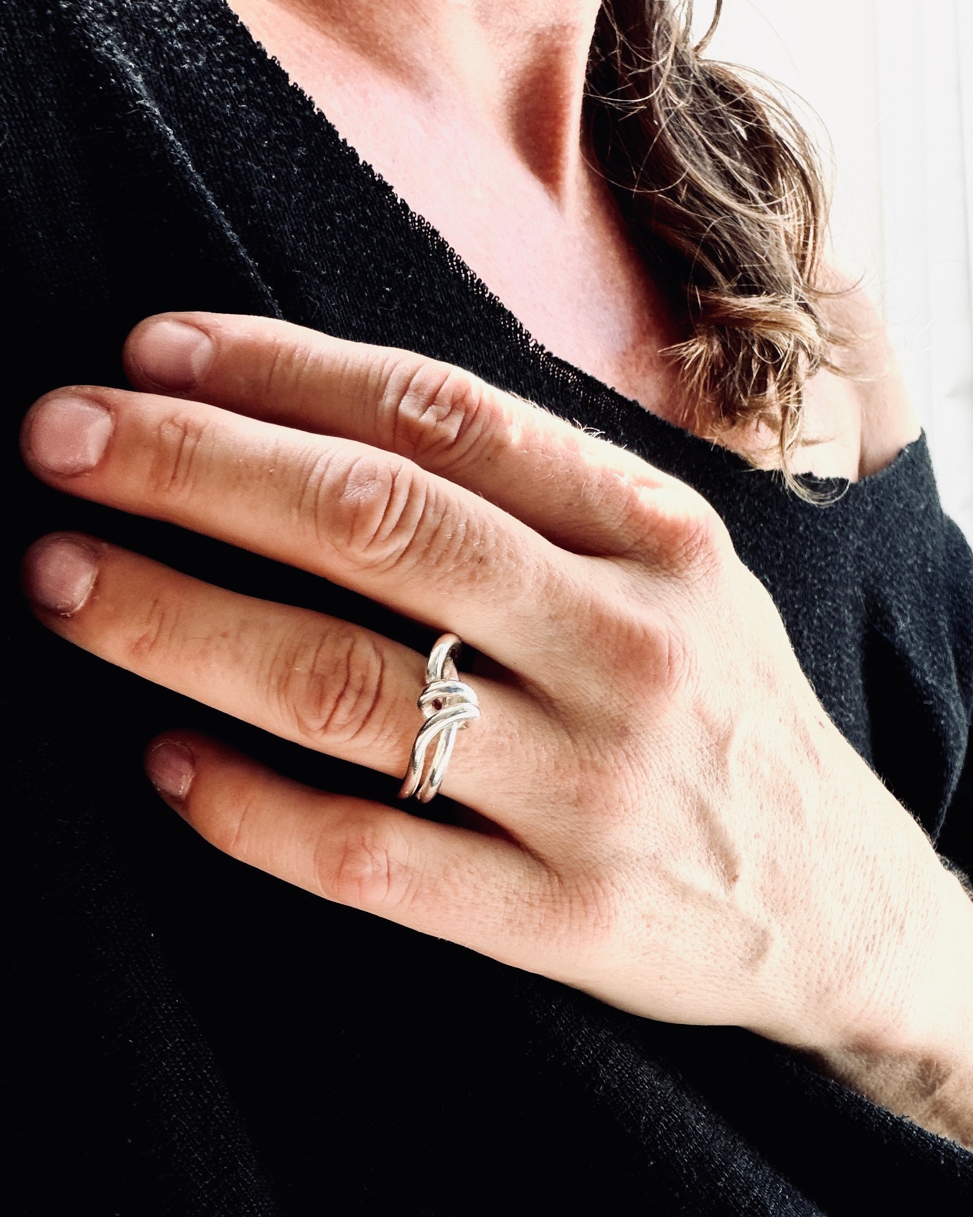 A close-up of a person's hand wearing a silver ring with a knotted design, set against a black knit top.
