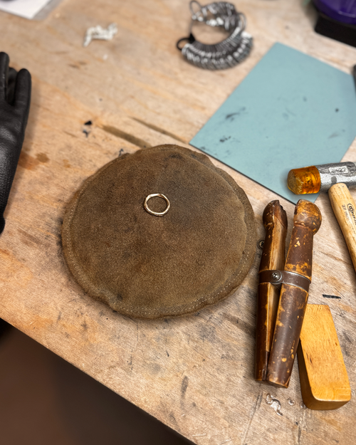 Gold ring sitting on leather circle in jewellery workshop surrounded by tools.