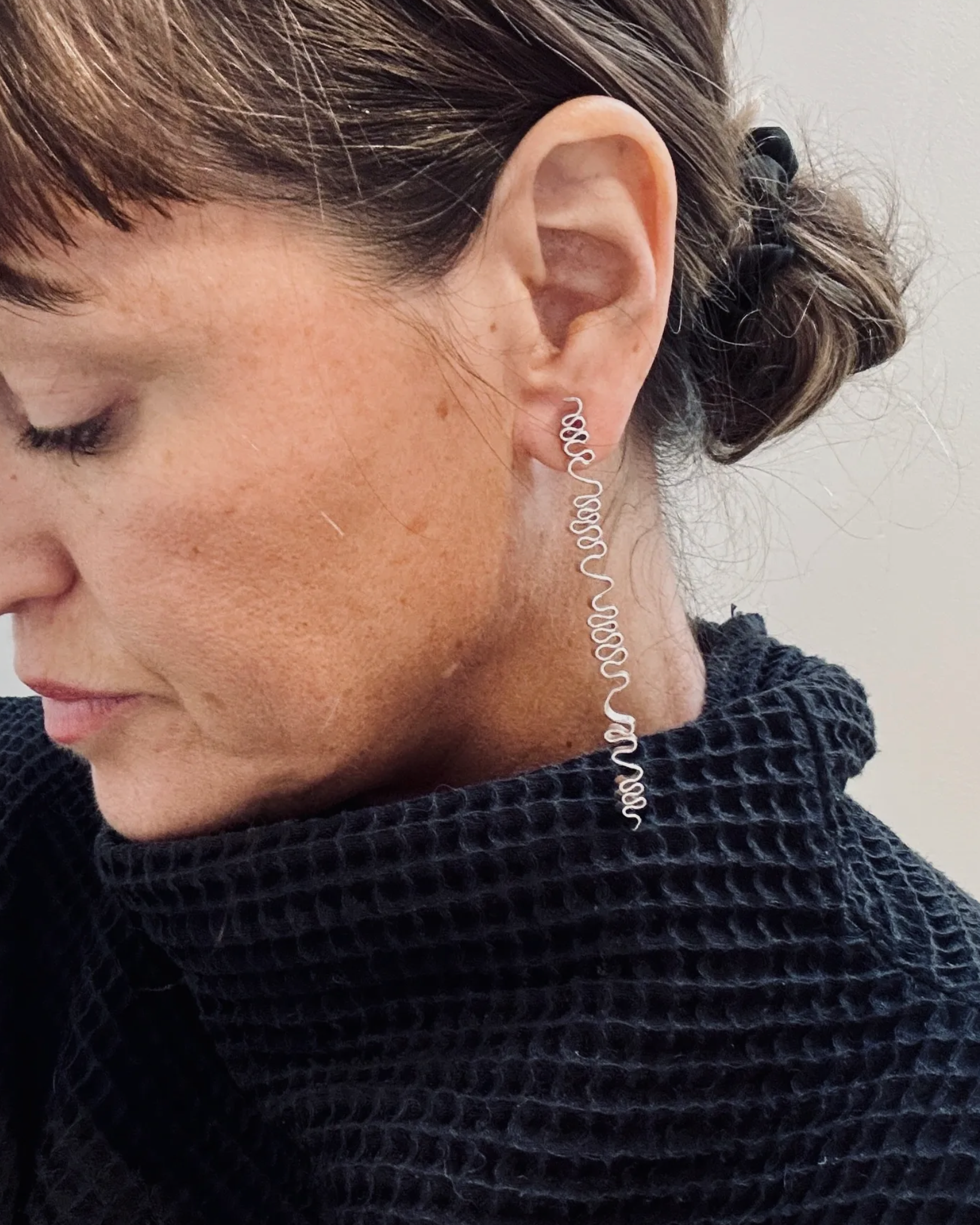 Close-up of a person wearing a silver spiral earring against a neutral background