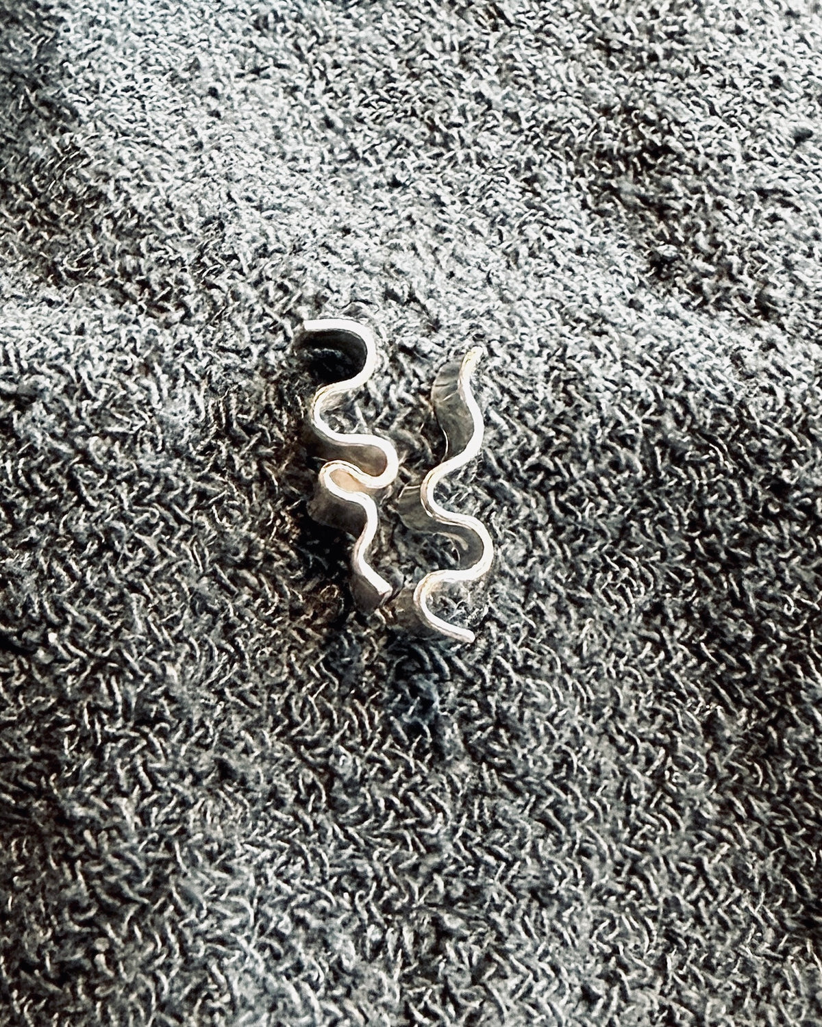 A pair of silver-toned spiral ear cuffs resting on a textured gray fabric background.