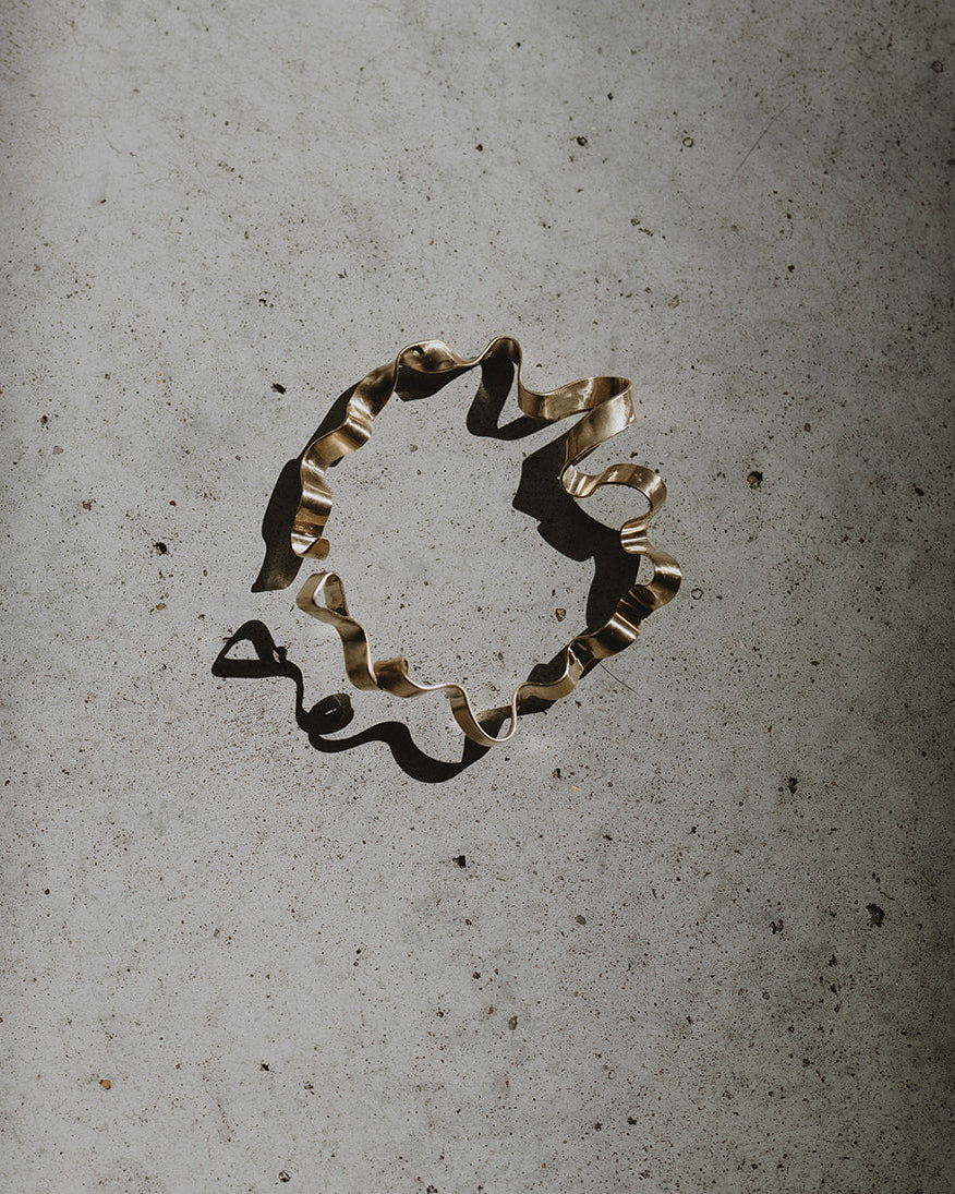 A single beige and brown ruffled ribbon or decorative strip lies on a textured light gray surface under dramatic directional light, casting a dark shadow.