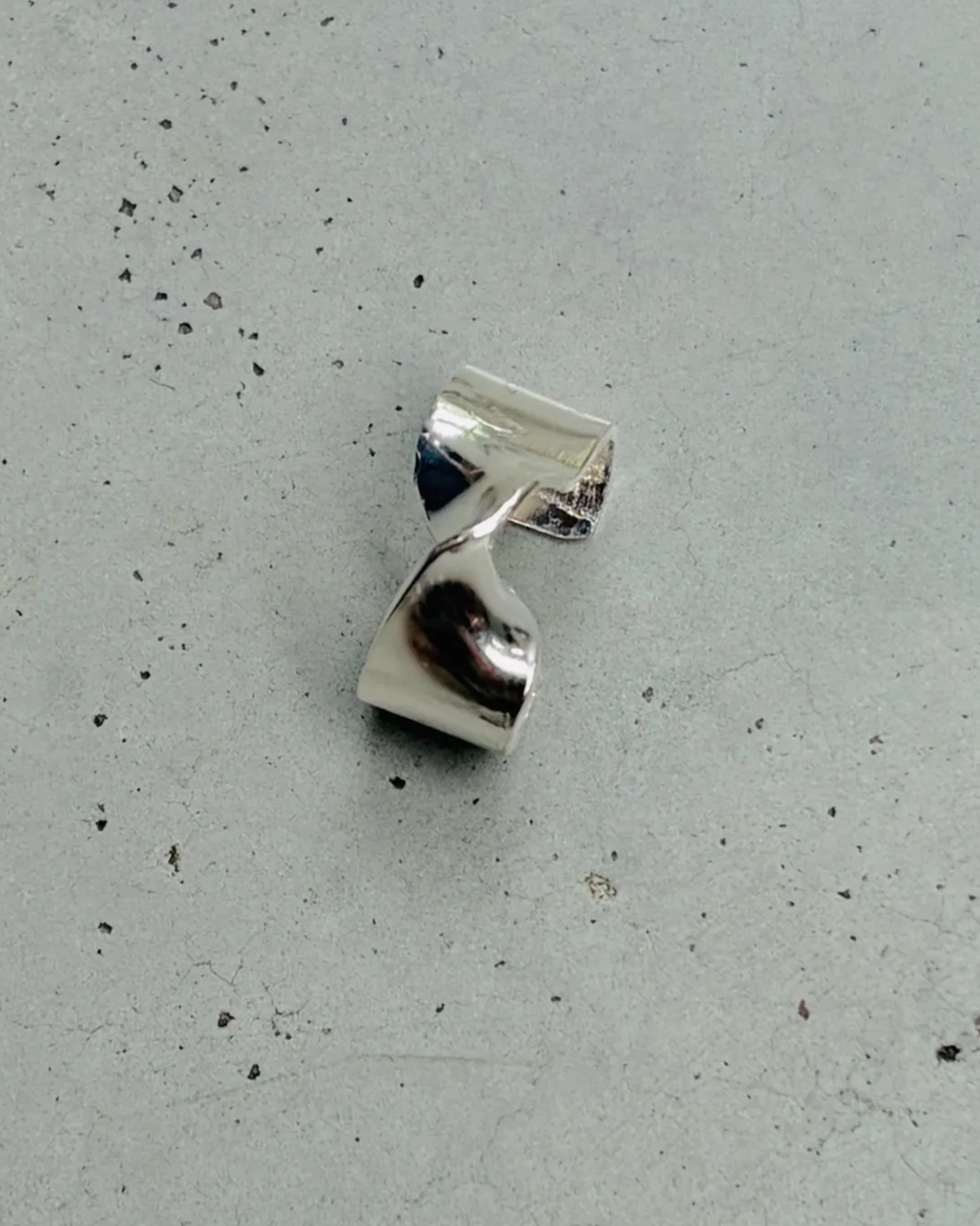 sculptural silver ear cuff sitting on concrete floor