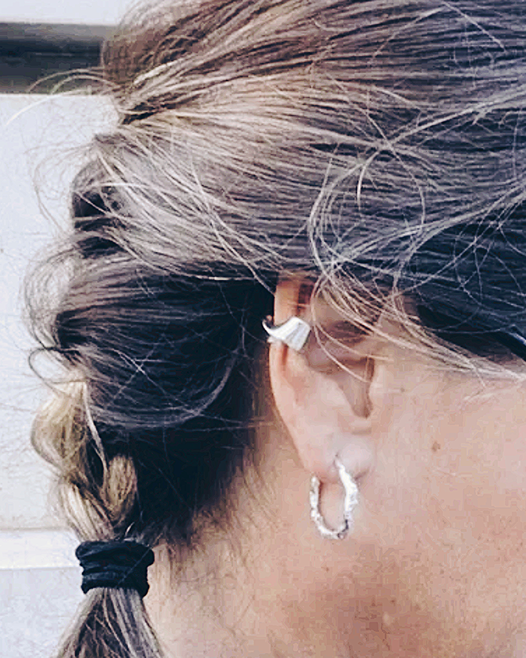close up of woman’s ear with braided hair with twisted silver ear cuff and silver hoops 