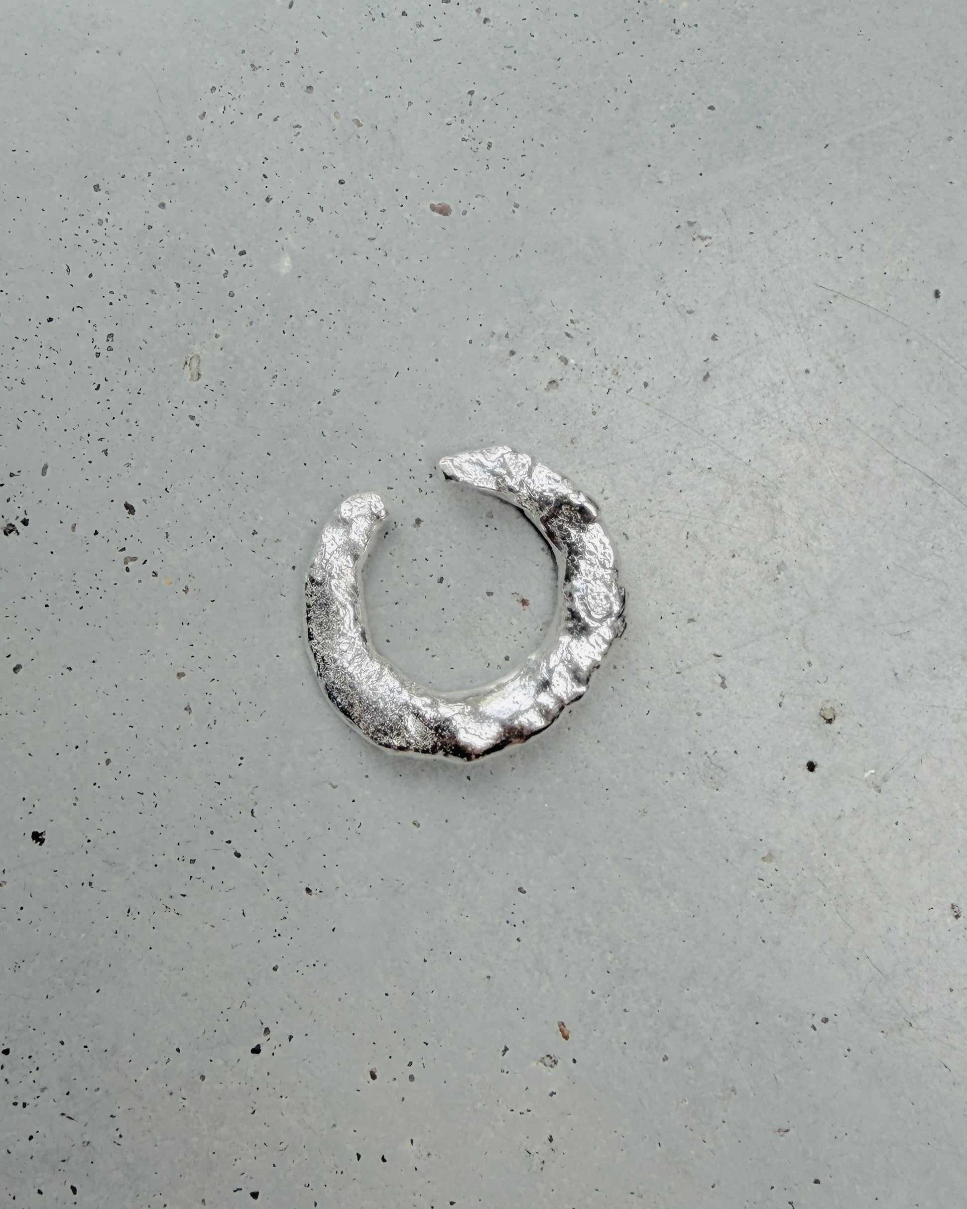 A single textured silver ring with a hammered finish, photographed on a speckled gray concrete surface.