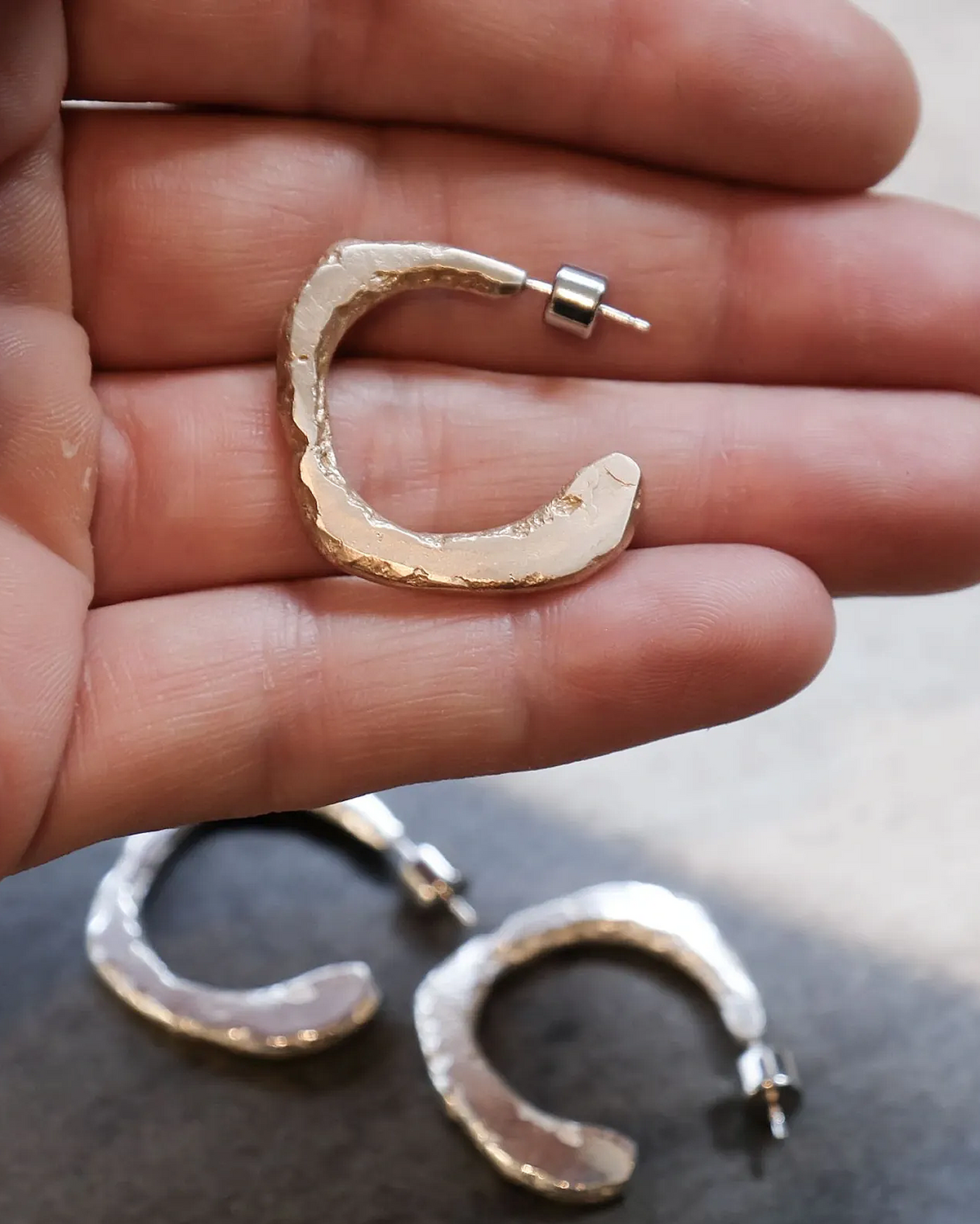 Gold hoop earrings held in a hand with a blurred background