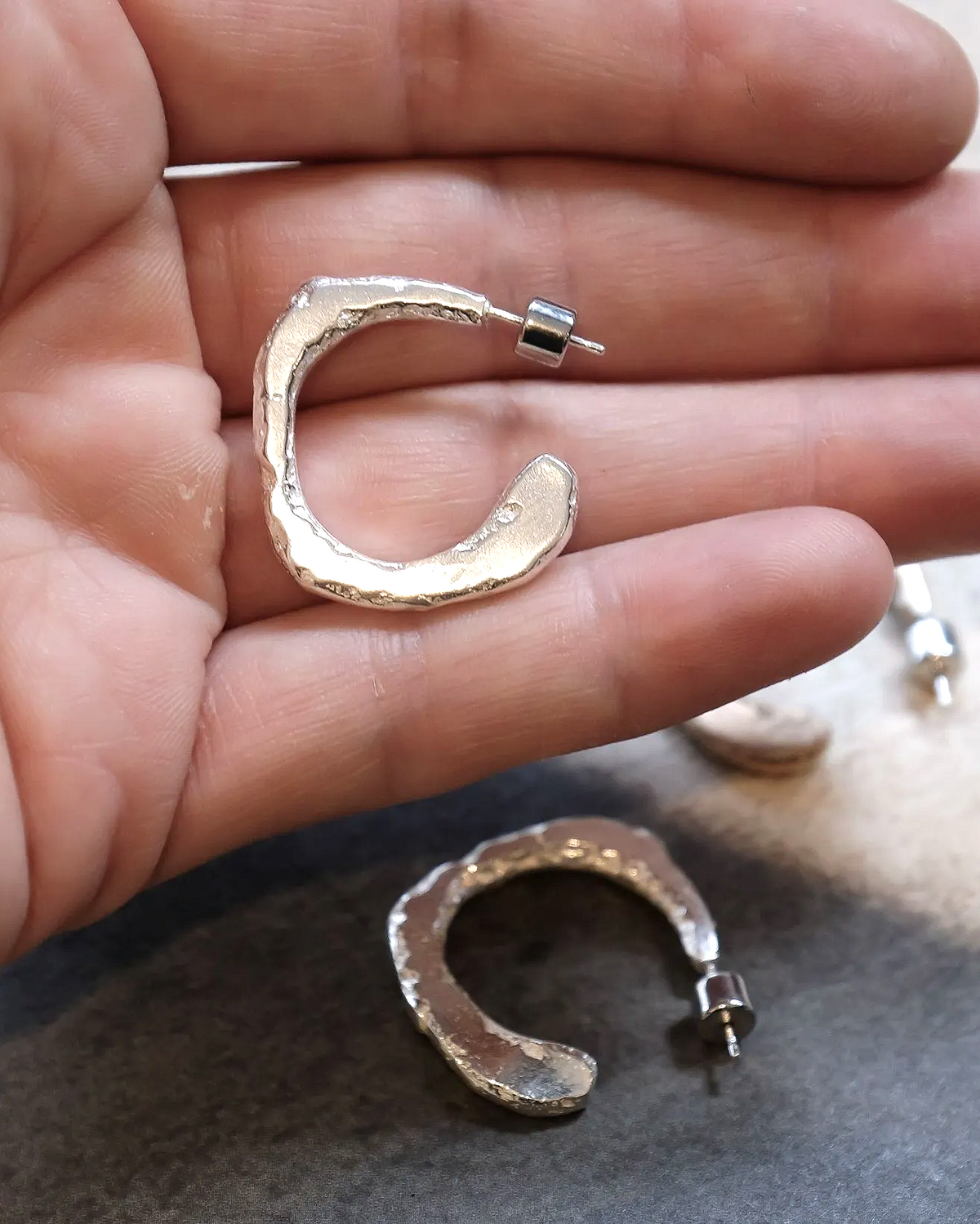 Gold hoop earrings held in a hand with a neutral background