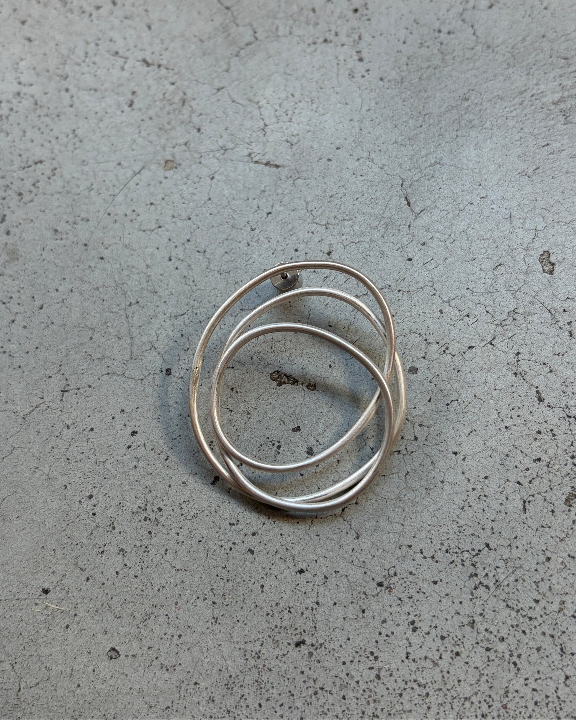 Three thin overlapping silver rings on a textured gray concrete surface.