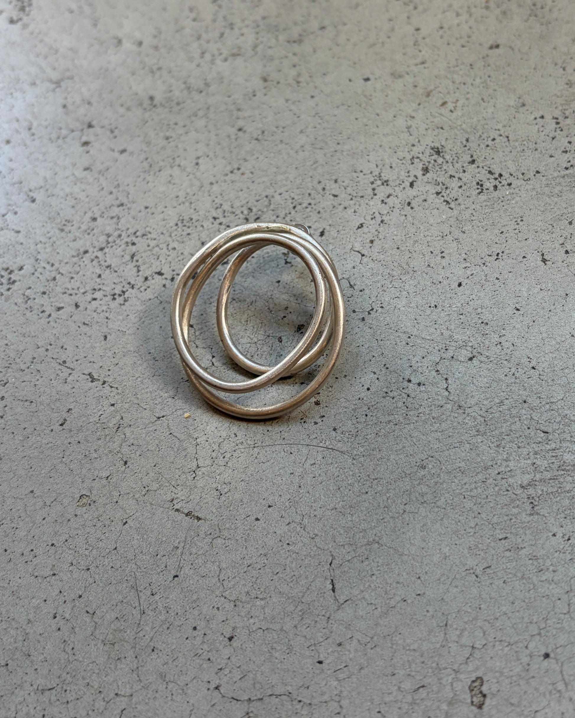 A pair of thin silver rings interlocked, resting on a textured gray concrete surface.