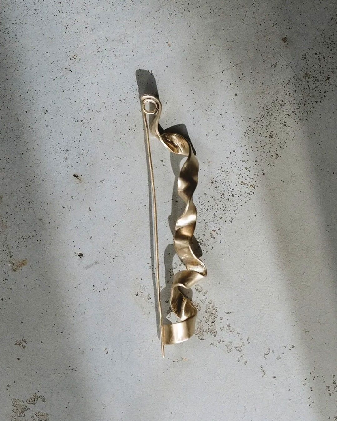 Gold brooch with a twisted design on a textured gray background
