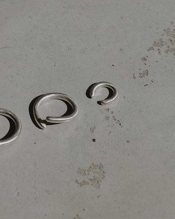 Three small silver metal jump rings of varying sizes arranged on a textured gray surface.