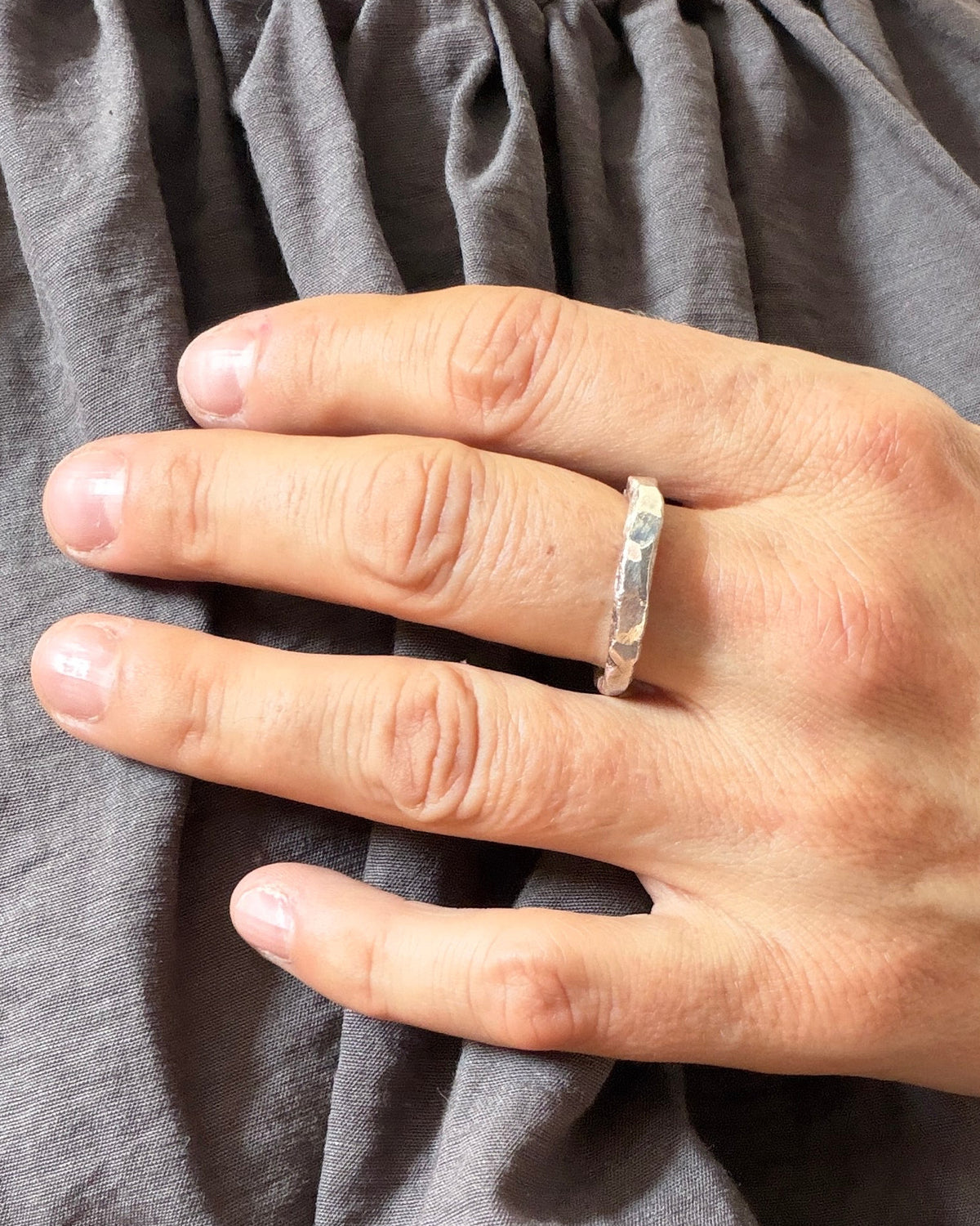A close-up of a person's hand wearing a textured silver band ring, resting on a dark gray linen top.