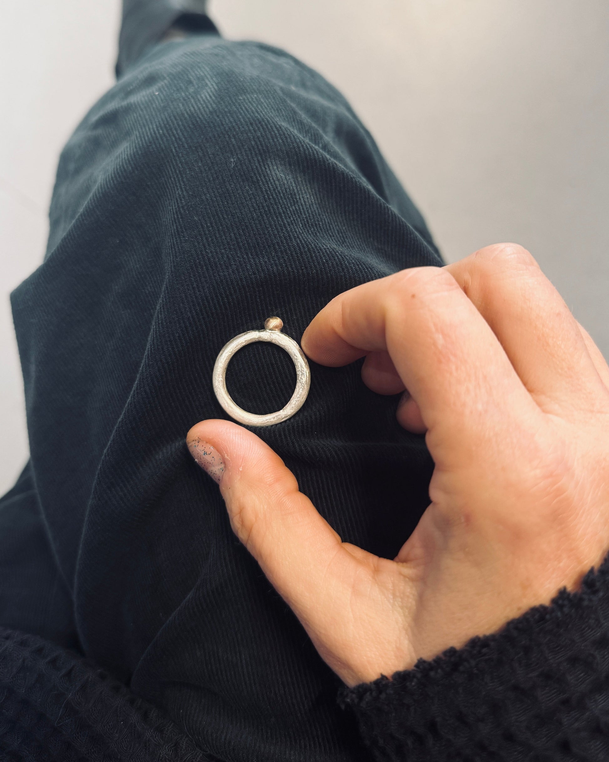 Hand holding a small circular object against a dark fabric background