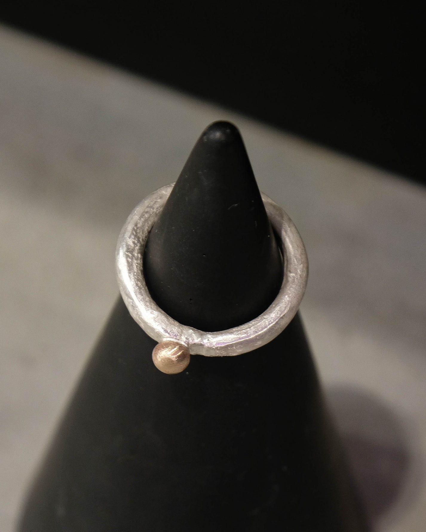 Silver ring with a small gold ball on a black cone against a gray background