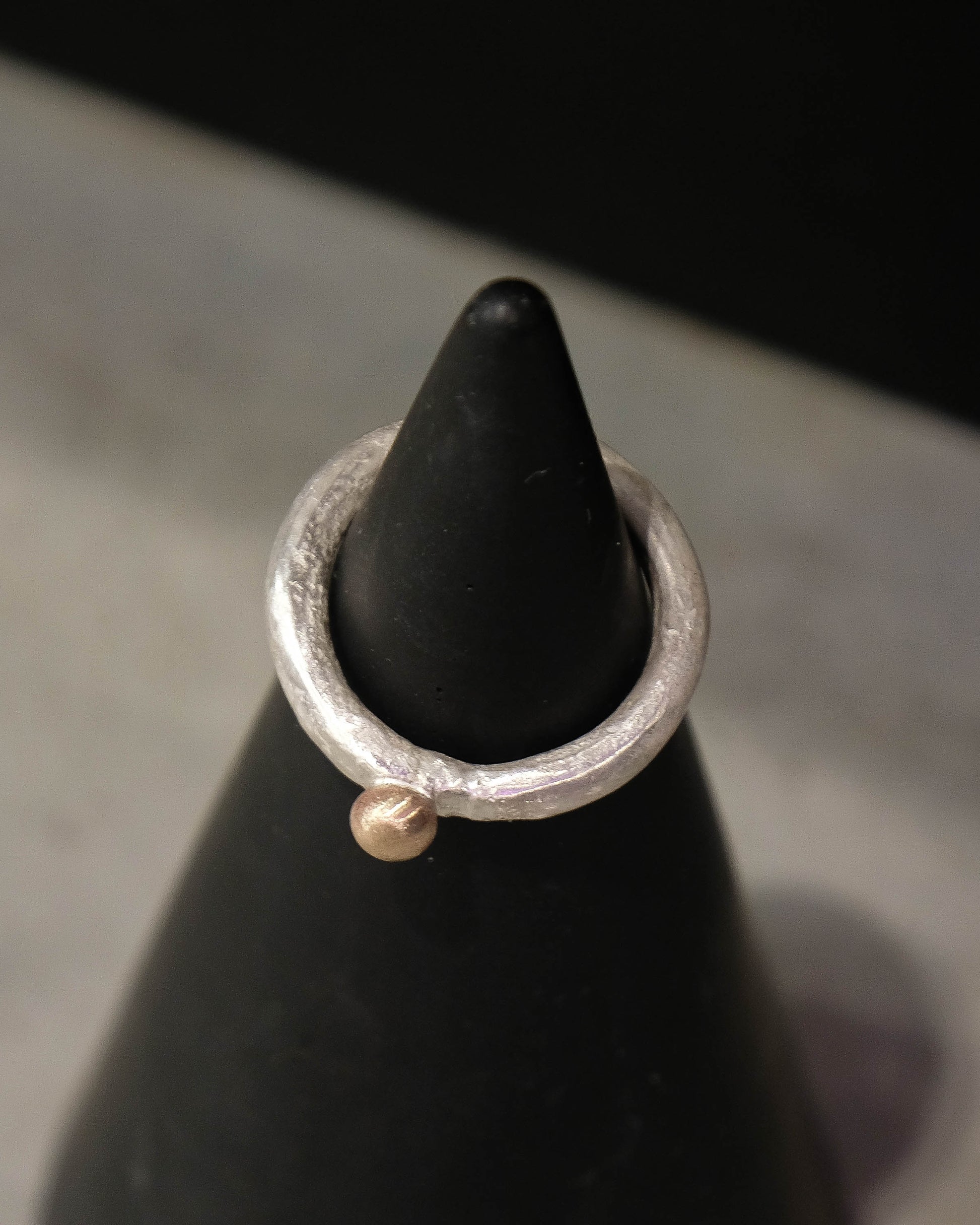 Silver ring with a small gold ball on a black cone against a gray background