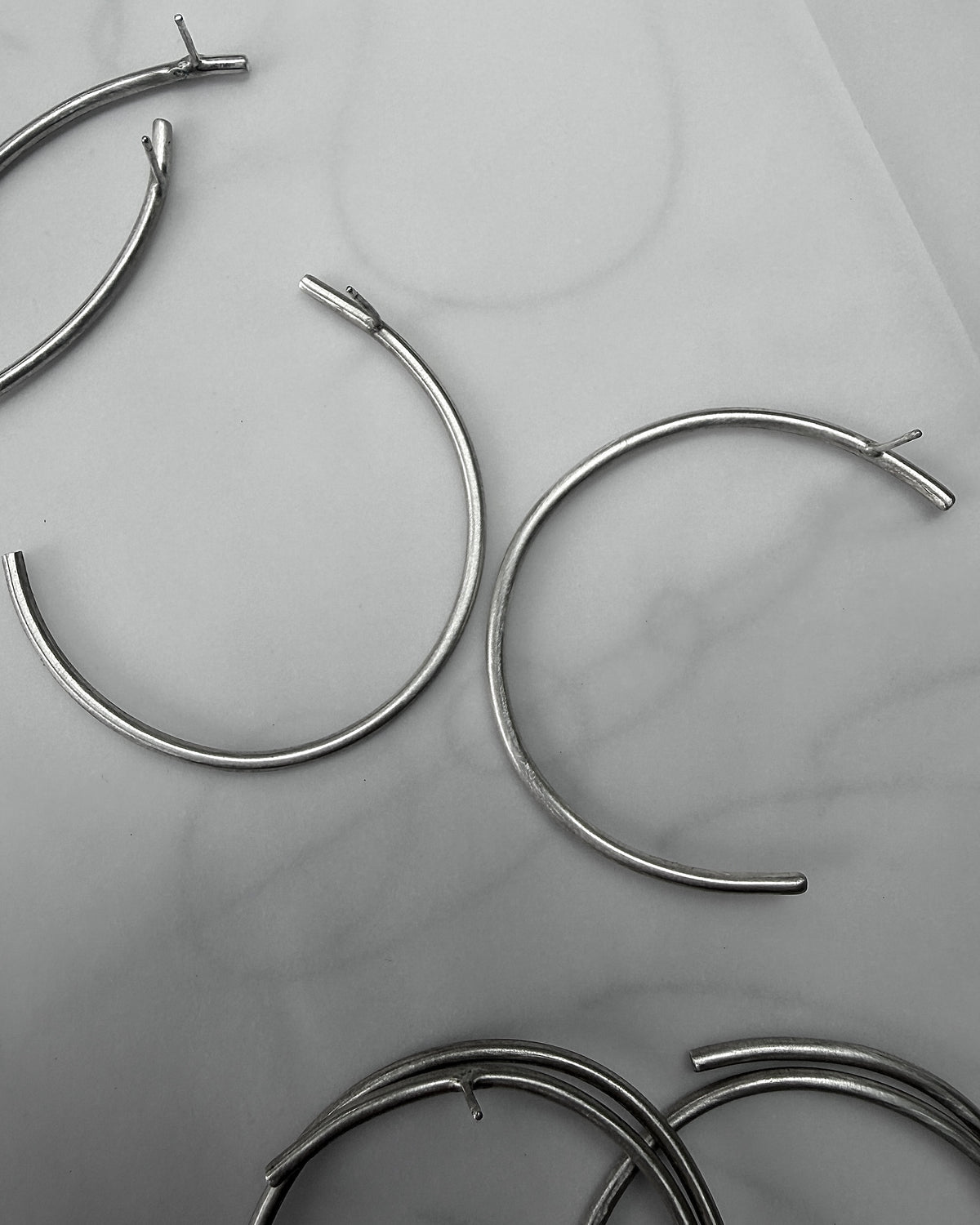 Several silver-toned metal hoop earrings with open ends are arranged on a light gray marble-like surface.