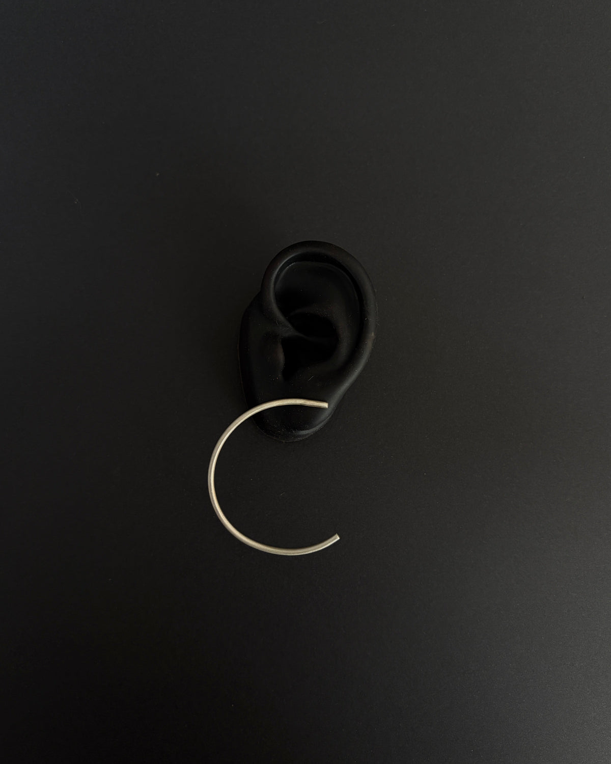 close up of silver arched earring on black silicone ear on black background