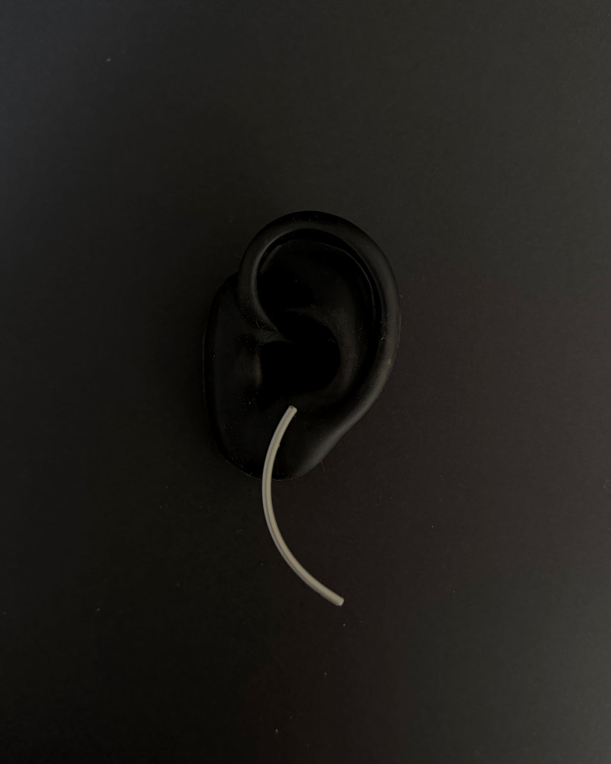 A black silicone ear-shaped object with a curved white tube extending downward, photographed against a dark black background.