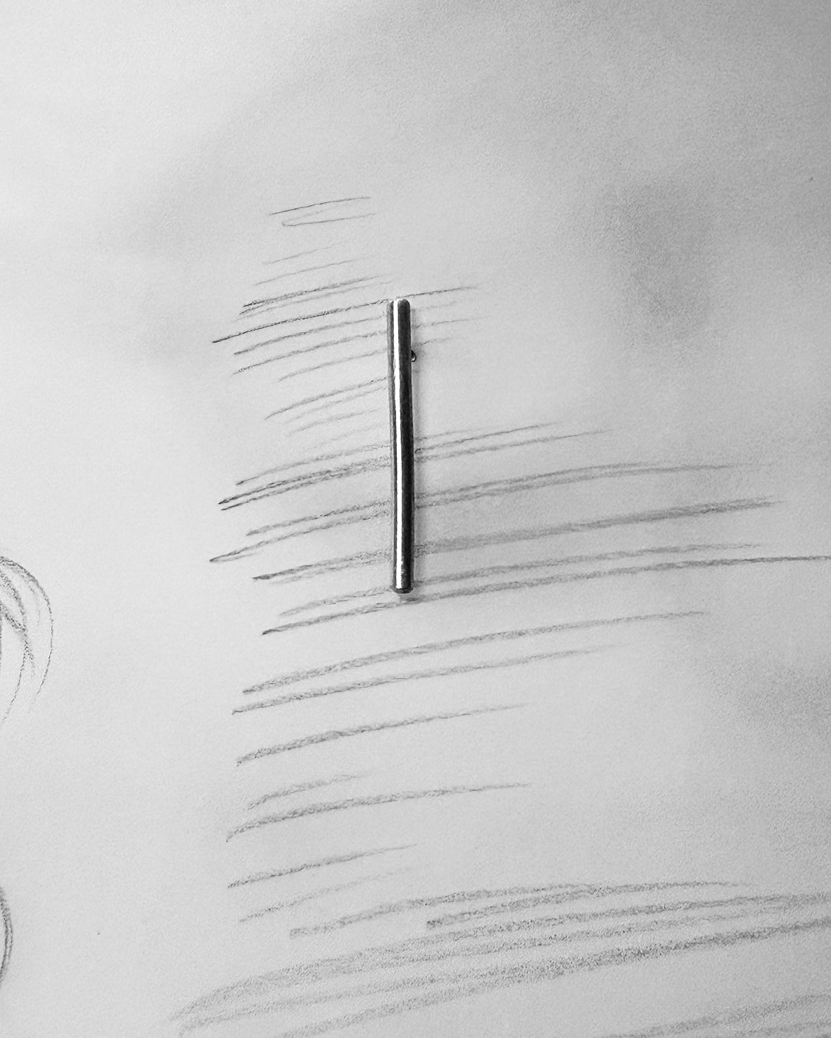 A slim, dark metallic bar pin or hair accessory centered on a white sheet of paper with pencil sketch lines.