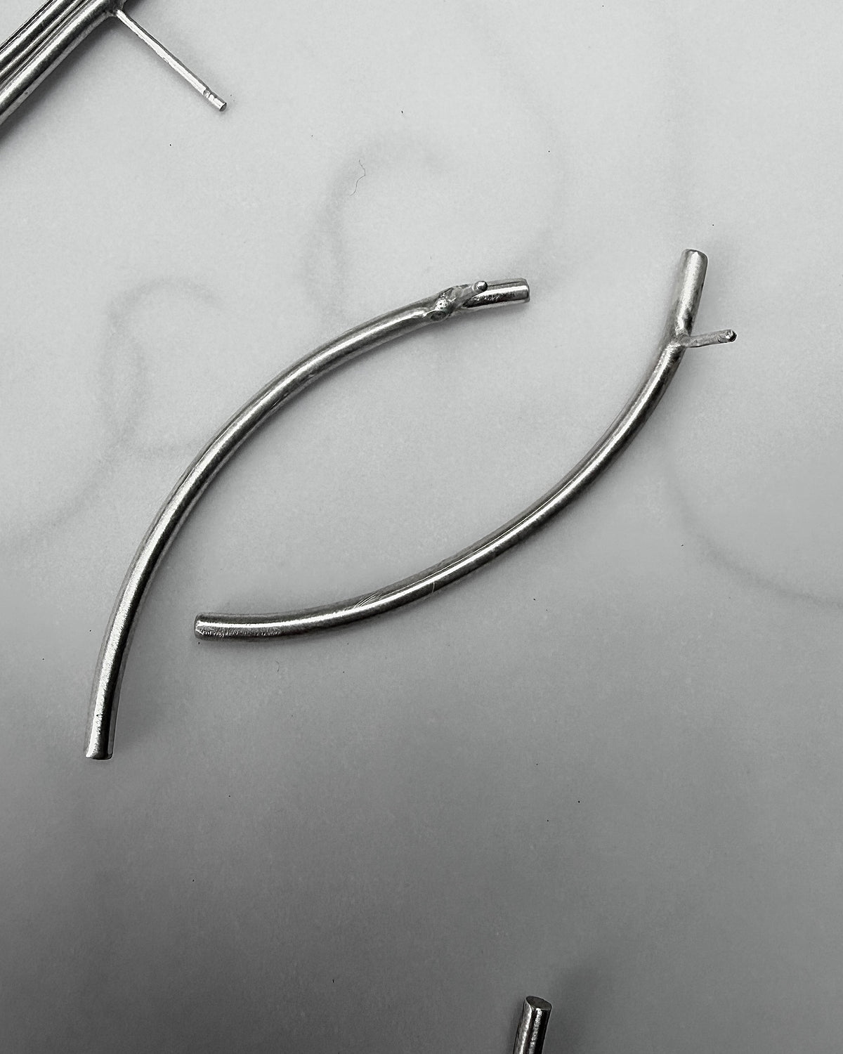 Two curved silver metal wire pieces with small flat ends, photographed on a light gray surface.