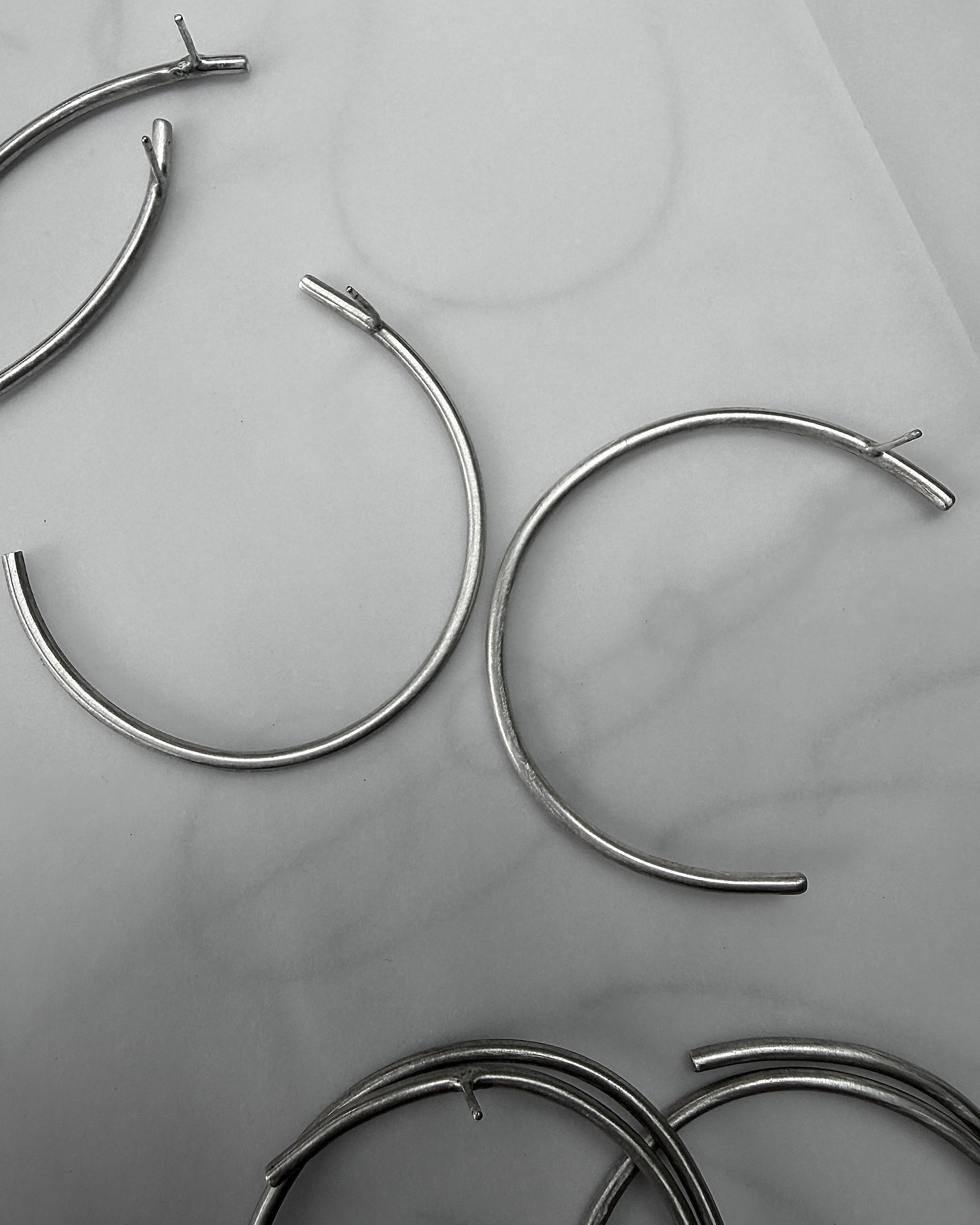 Several silver-toned metal hoop earrings with open ends are arranged on a light gray marble-like surface.
