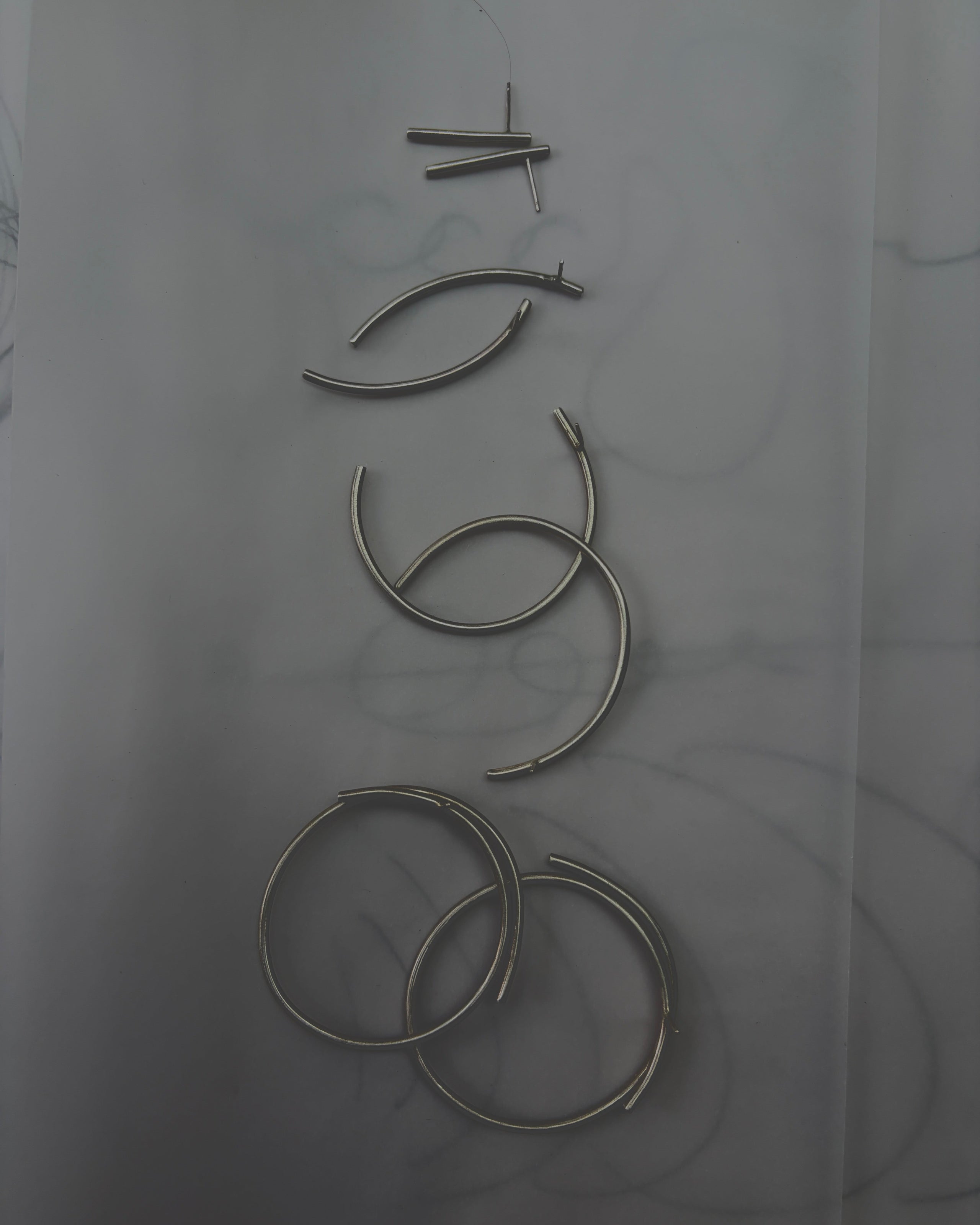 Six silver-toned metal ear cuffs or hoop-style ear pieces arranged vertically on a light gray marble-like surface.