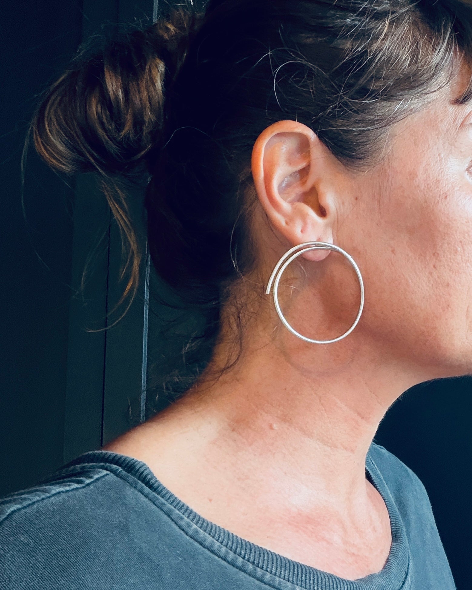 A close-up side profile of a woman wearing a pair of large, thin silver hoop earrings.