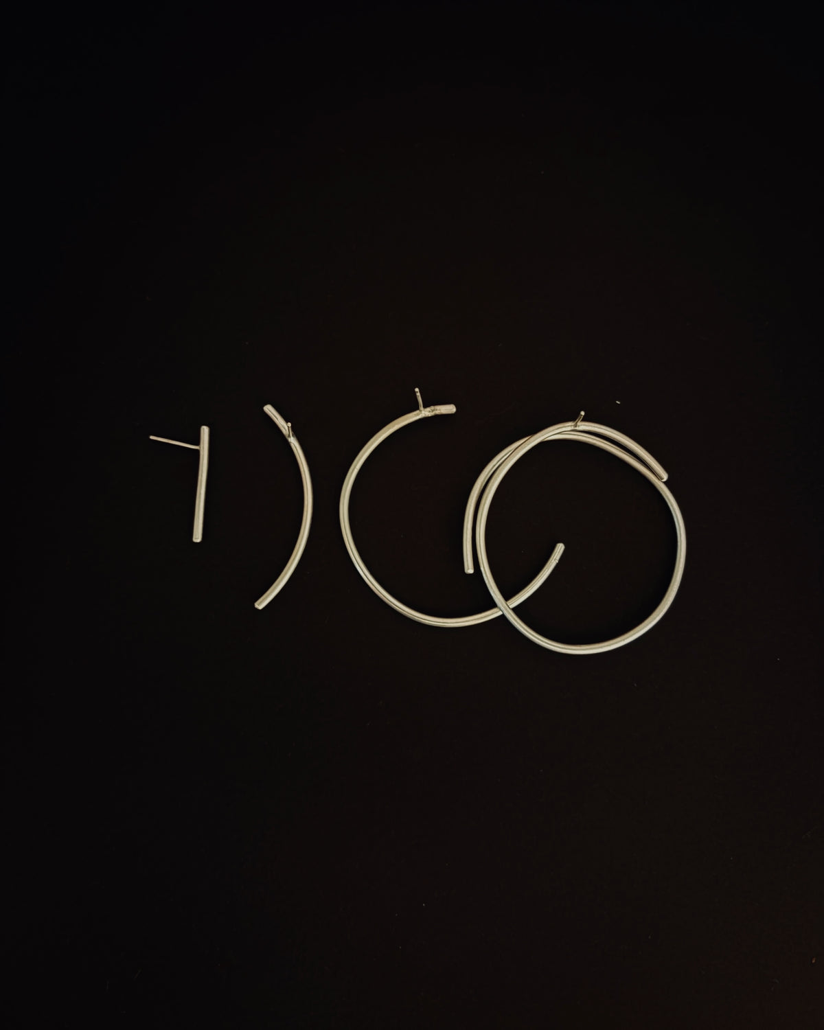 Three pairs of thin metal wire hoop earrings in different sizes, arranged on a solid black background.