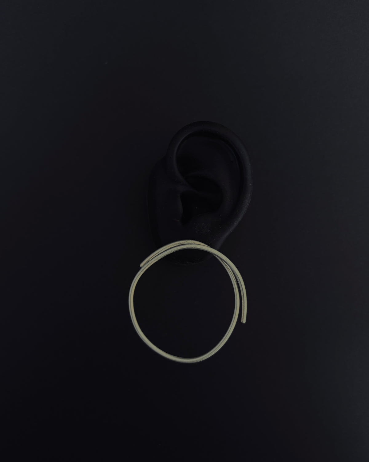 A single large, thin silver-toned hoop earring displayed against a dark, matte black background.