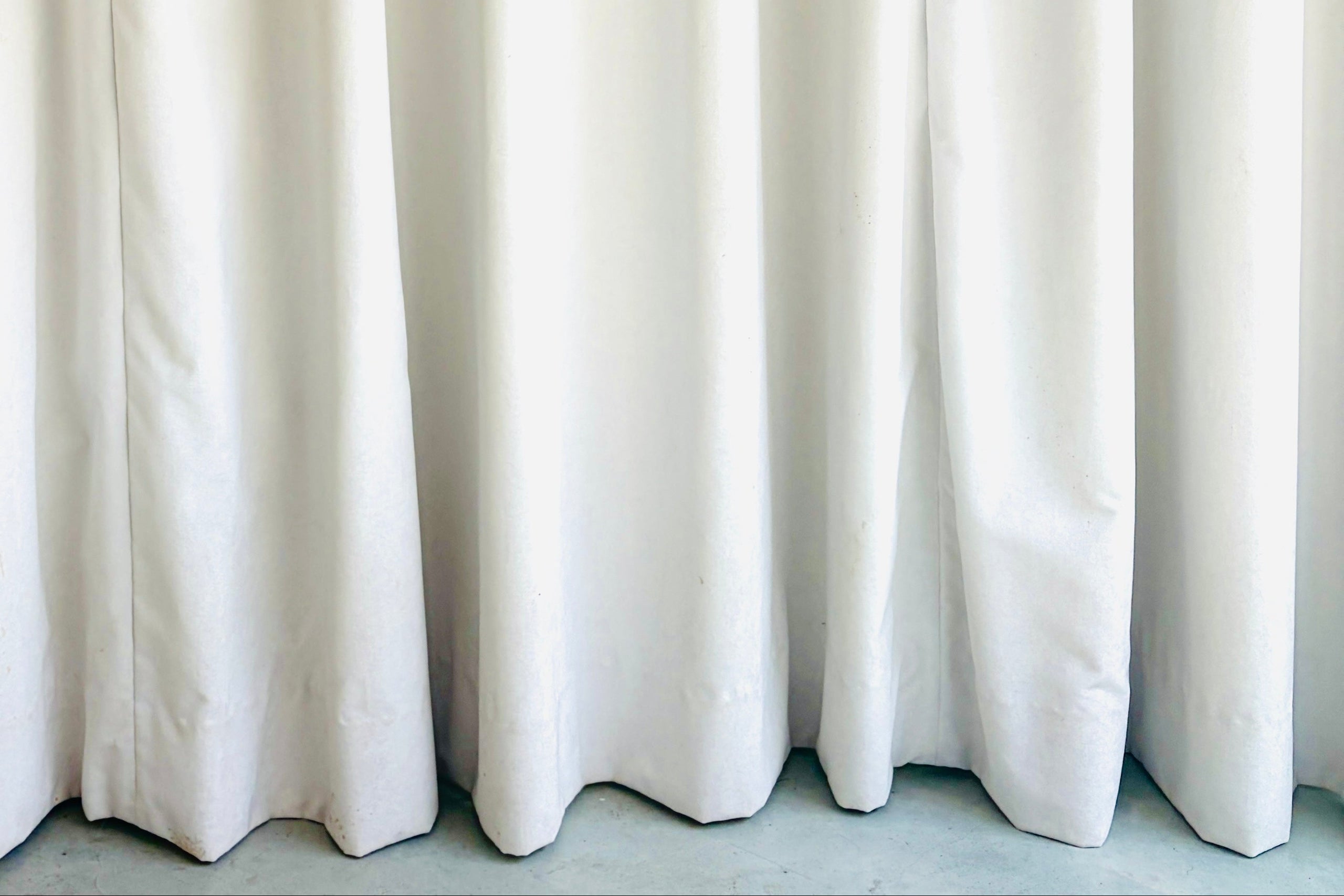 White curtain panels hanging down, showing soft vertical folds and a light gray concrete floor at the bottom.