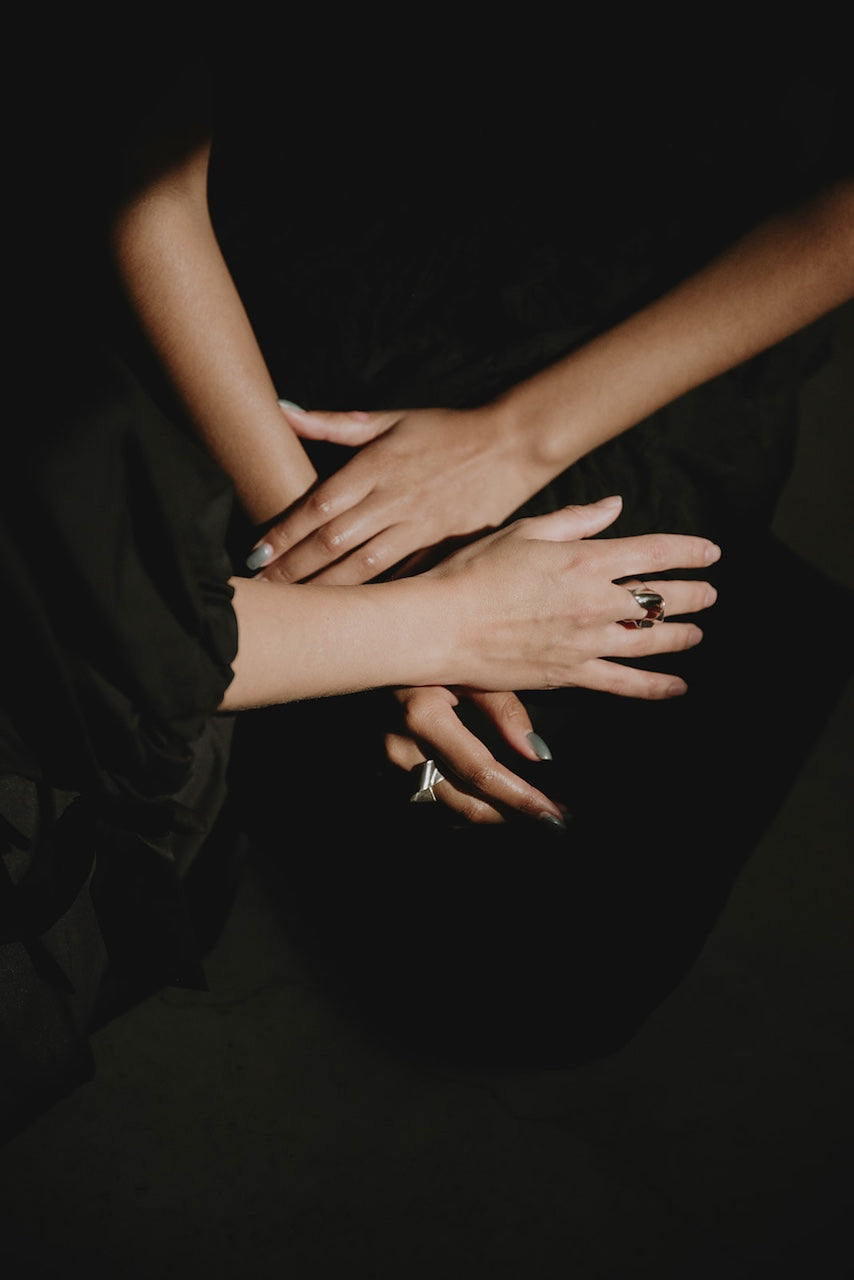 Close-up of stacked hands wearing rings against a dark background.